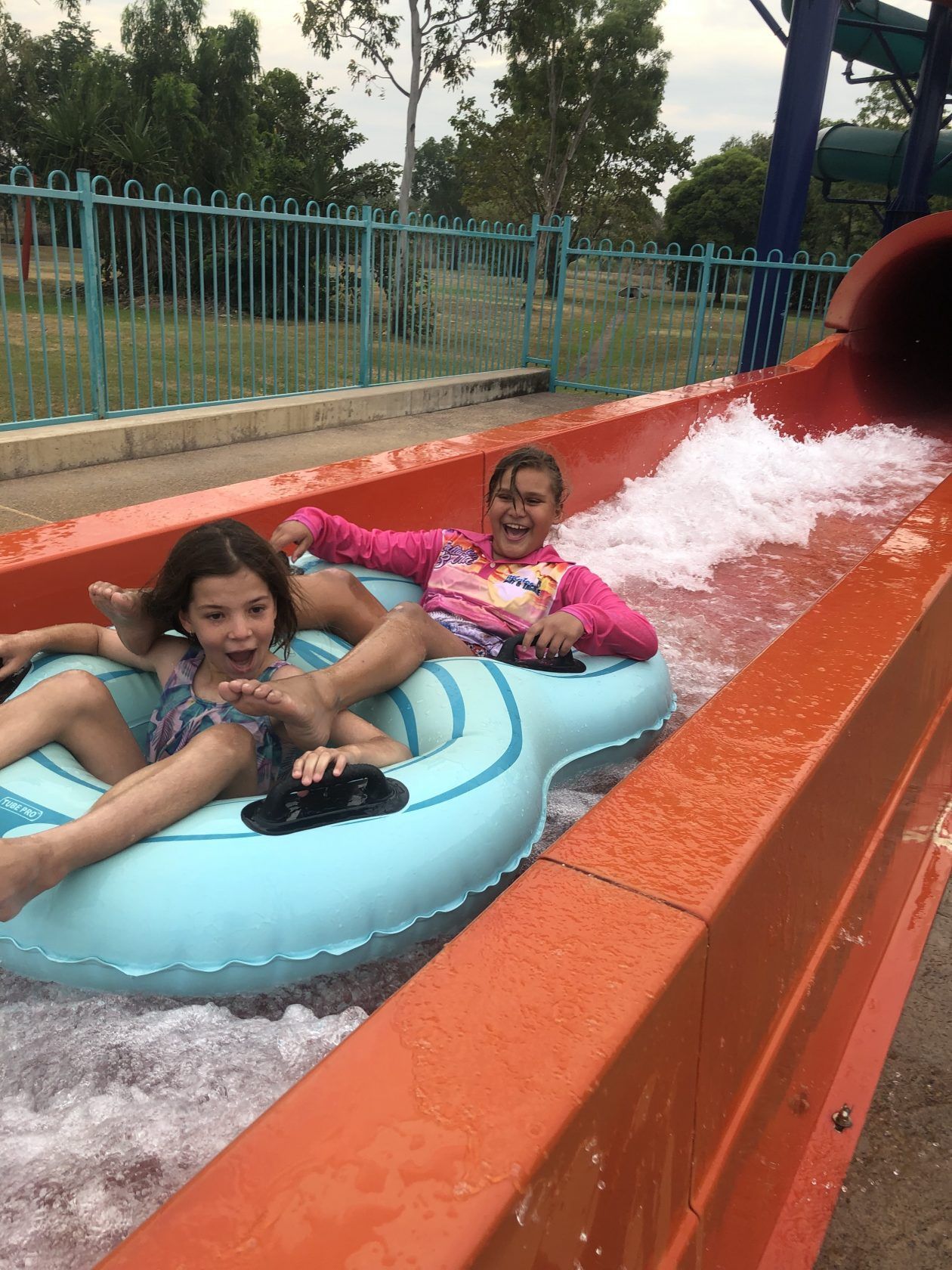 Two young girls are riding a water slide at a water park.