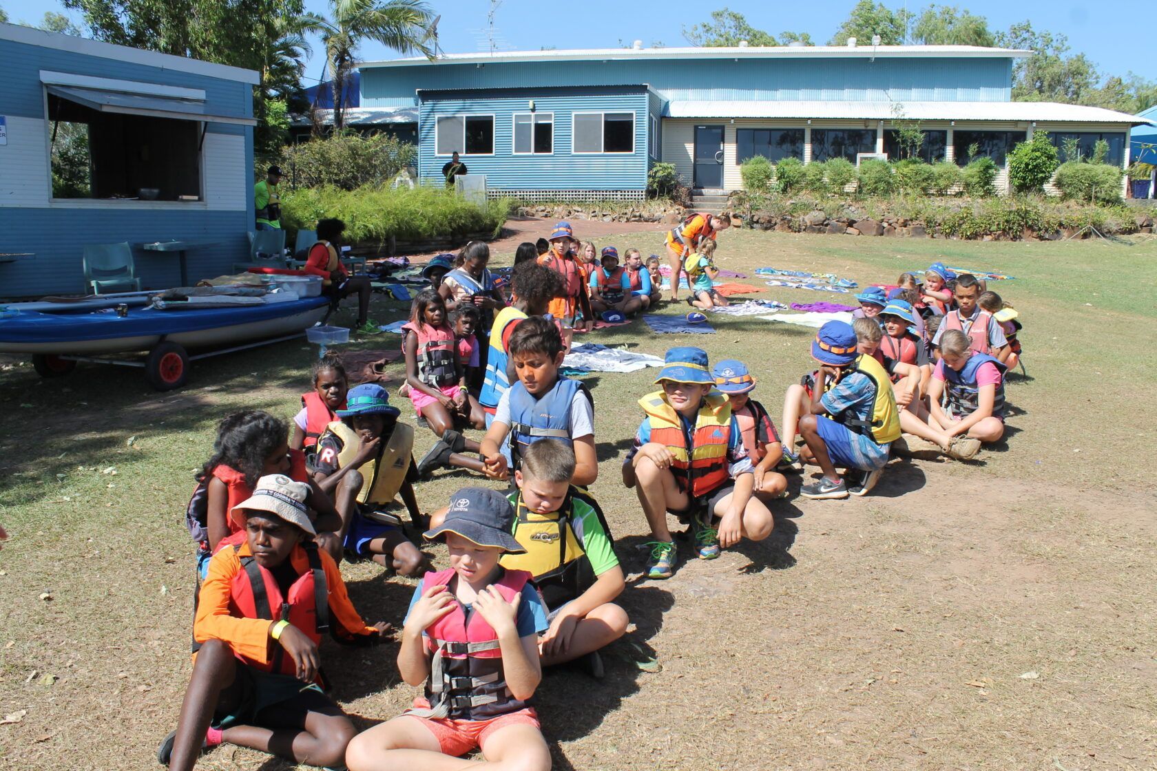 A group of children are sitting on the ground in front of a building.