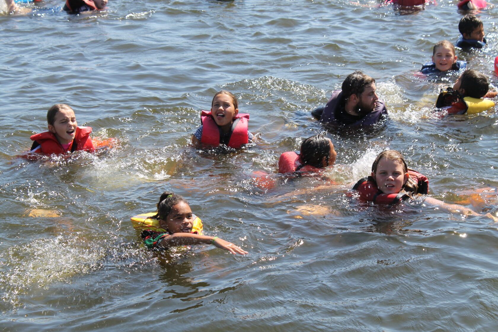 A group of children wearing life jackets are swimming in the water.