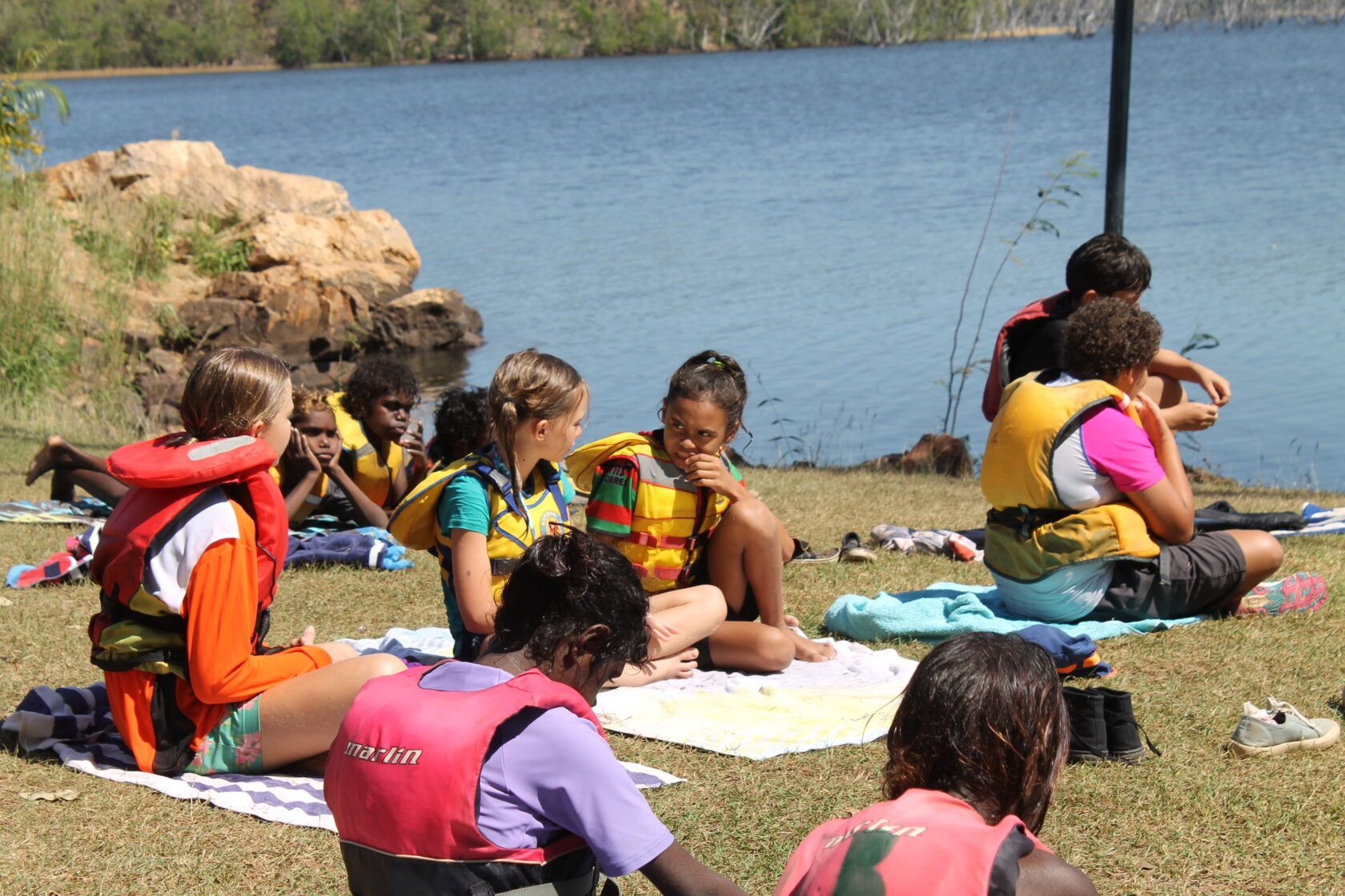 A group of children are sitting on the grass near a lake