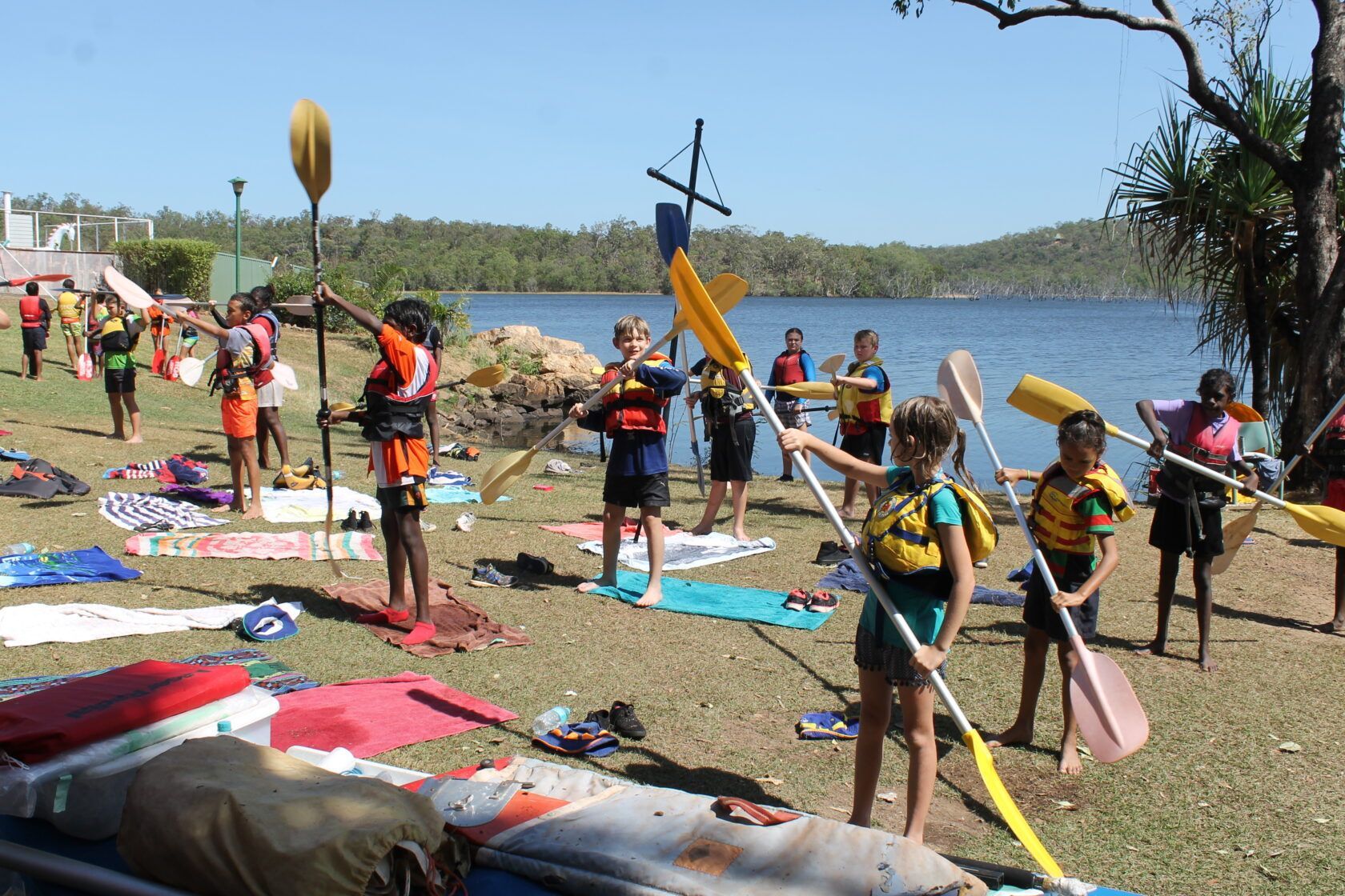 A group of people are standing on the shore of a lake holding paddles