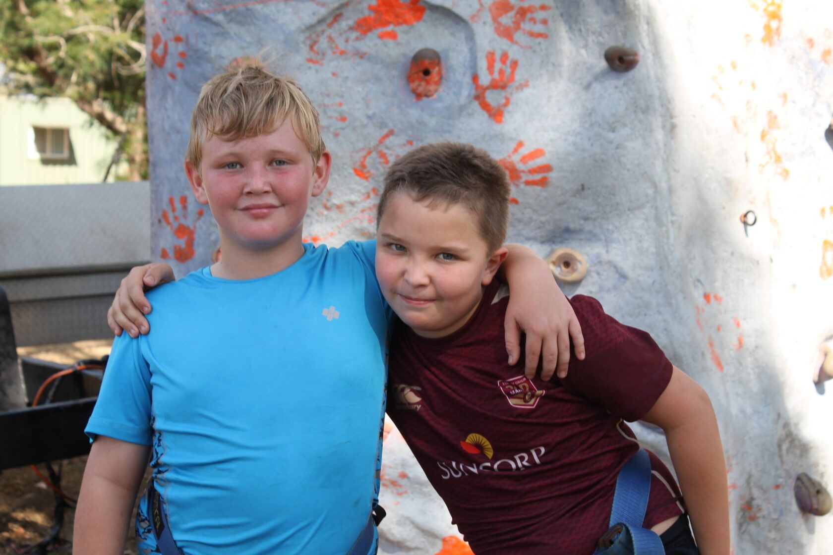 Two young boys are posing for a picture in front of a climbing wall.