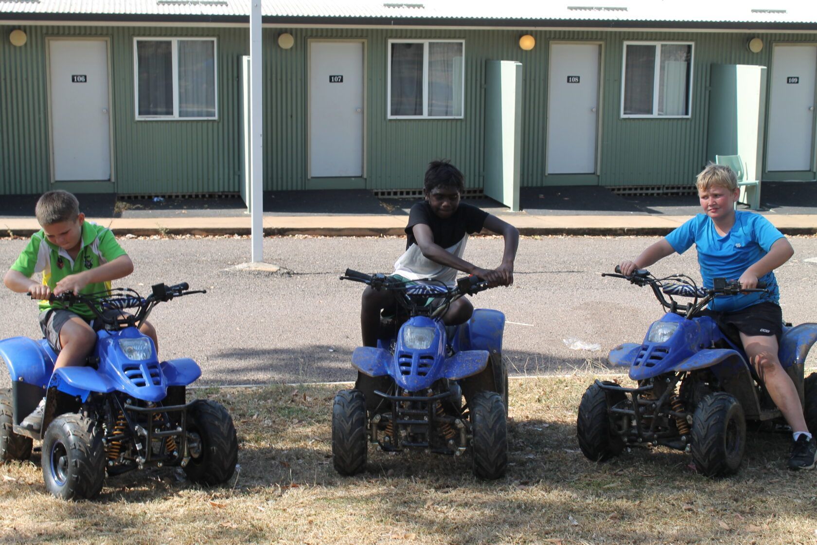 Three people are riding four wheelers in front of a building