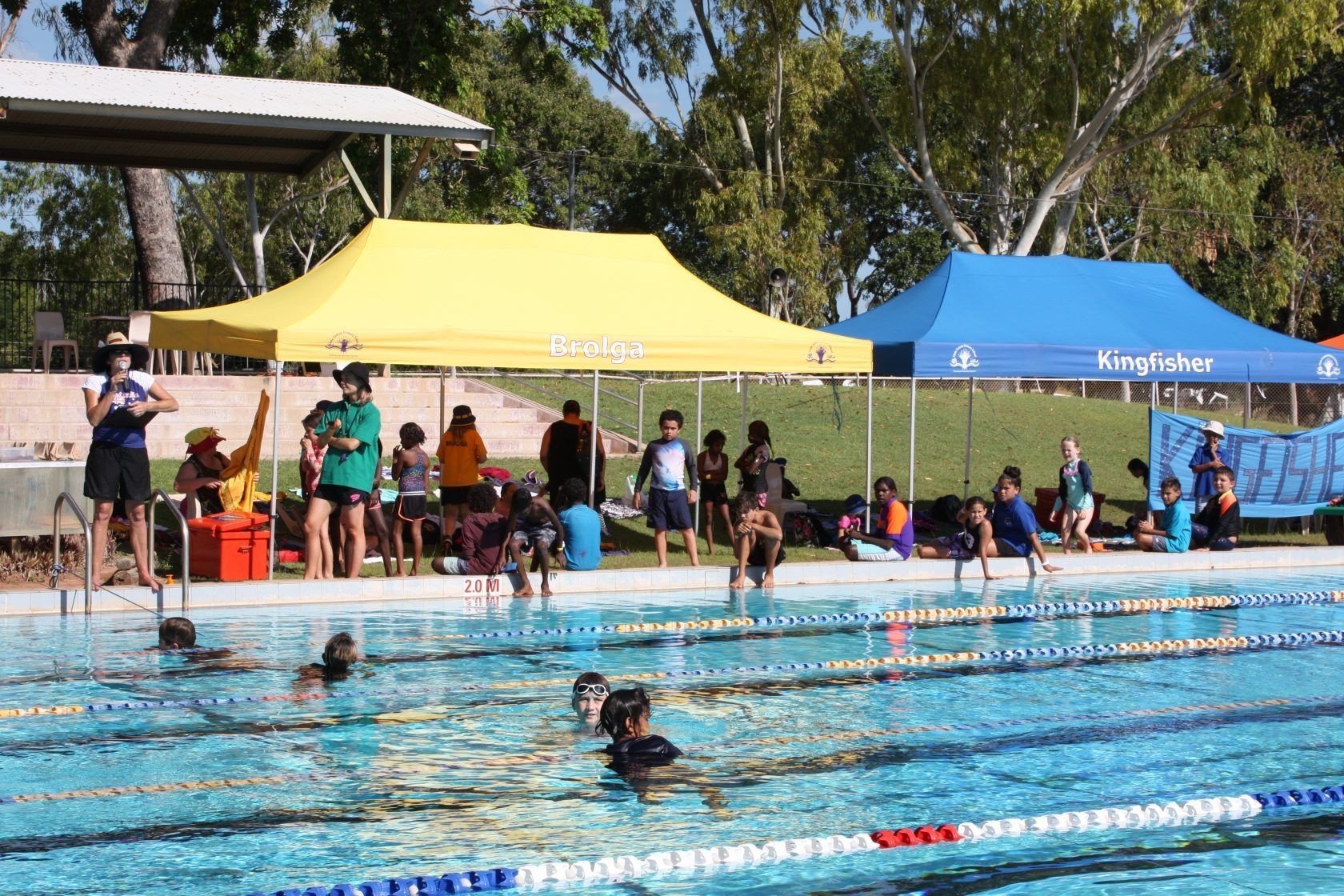 A group of people are swimming in a pool with tents in the background.