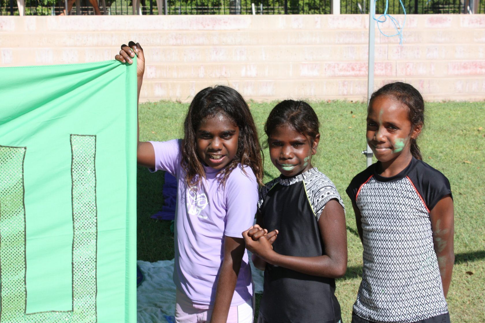 Three young girls are standing next to each other holding a green cloth.