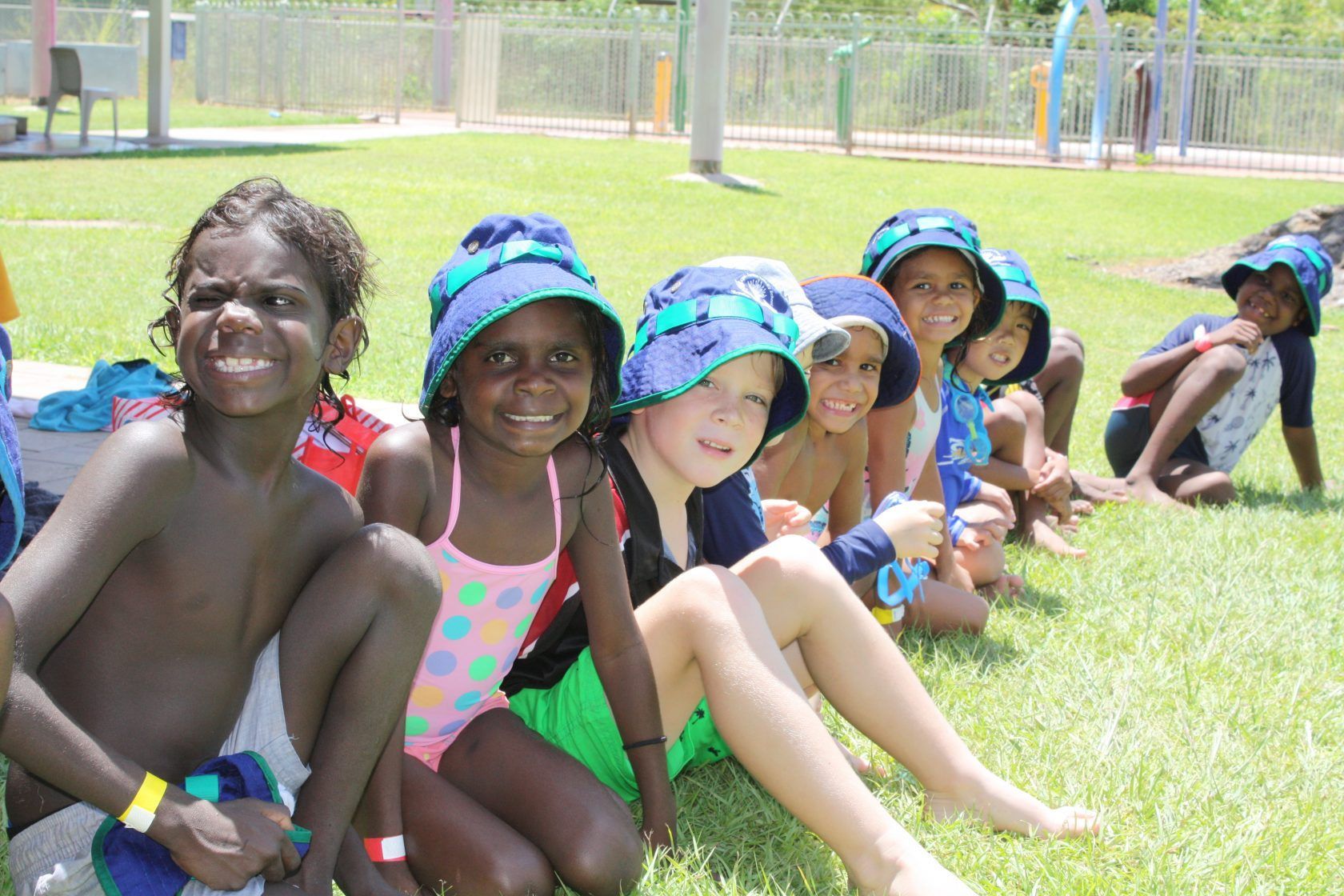 A group of children are sitting on the grass wearing hats.