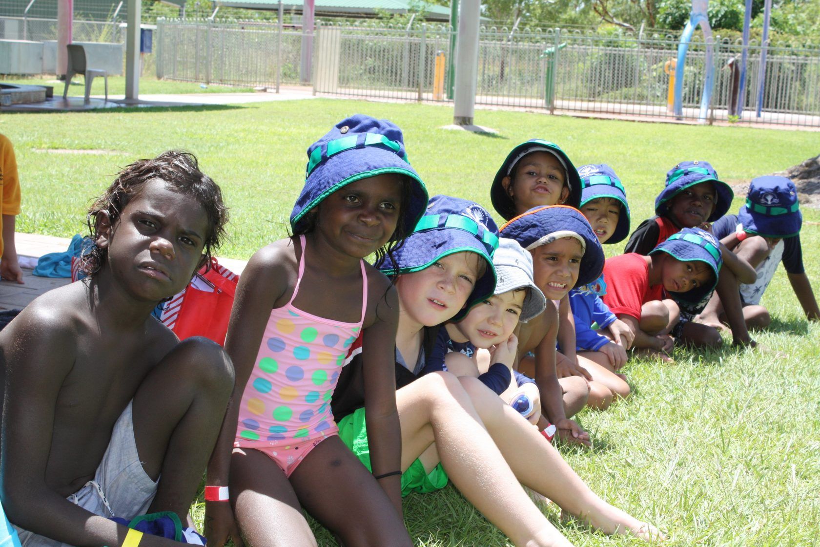 A group of children are sitting on the grass wearing hats