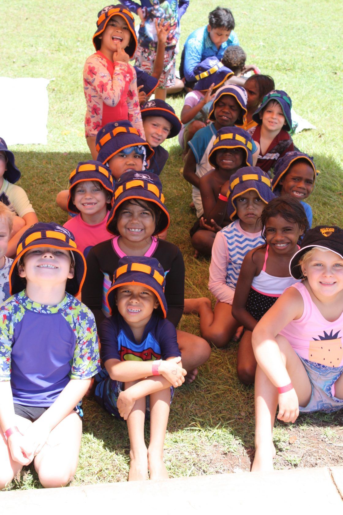 A group of children wearing hats are sitting on the grass