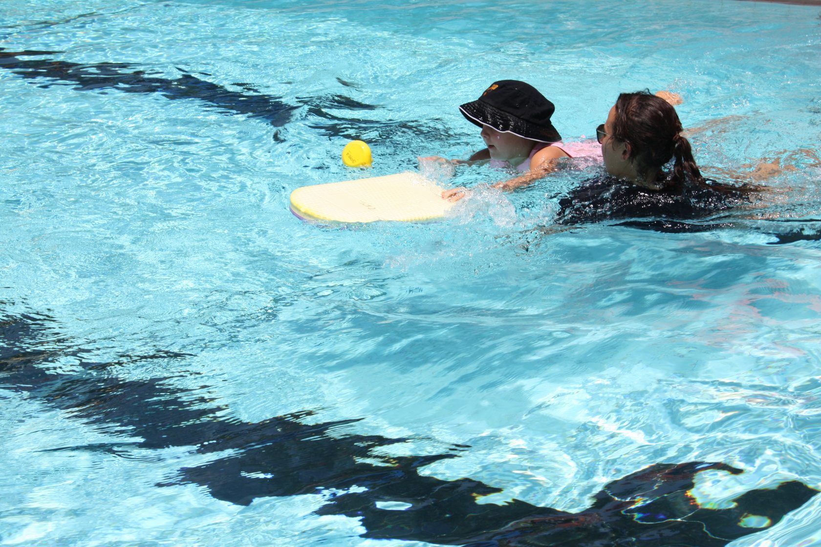 Two people are swimming in a pool with a yellow ball