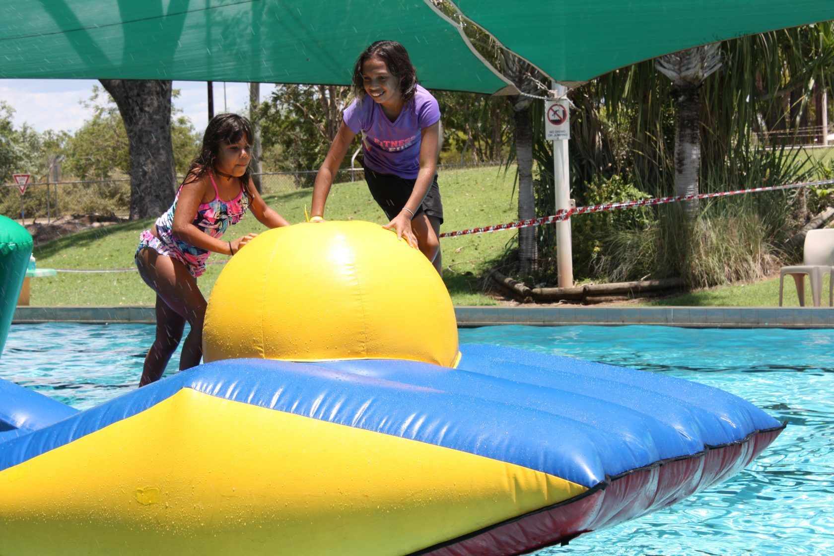 Two girls are playing with a large inflatable ball in a pool.