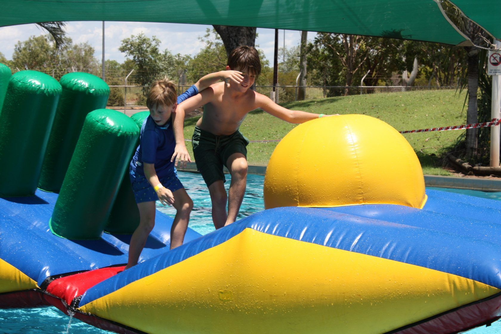 Two young boys are playing on an inflatable slide in a pool.