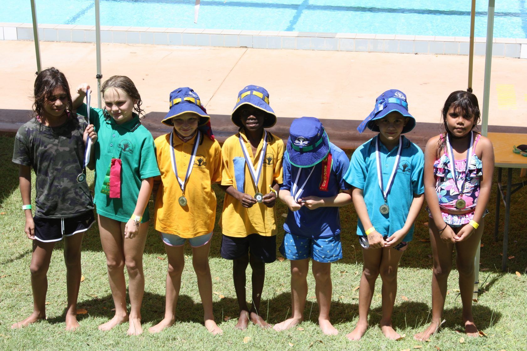 A group of children are posing for a picture in front of a pool.