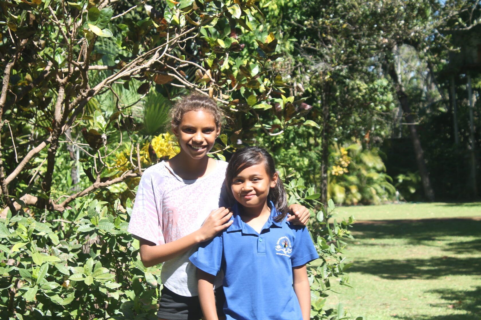 Two young girls are posing for a picture in front of a tree.