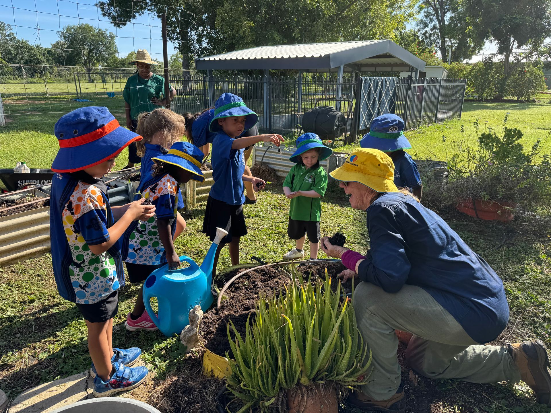 A group of children are playing in a garden with a man kneeling down.