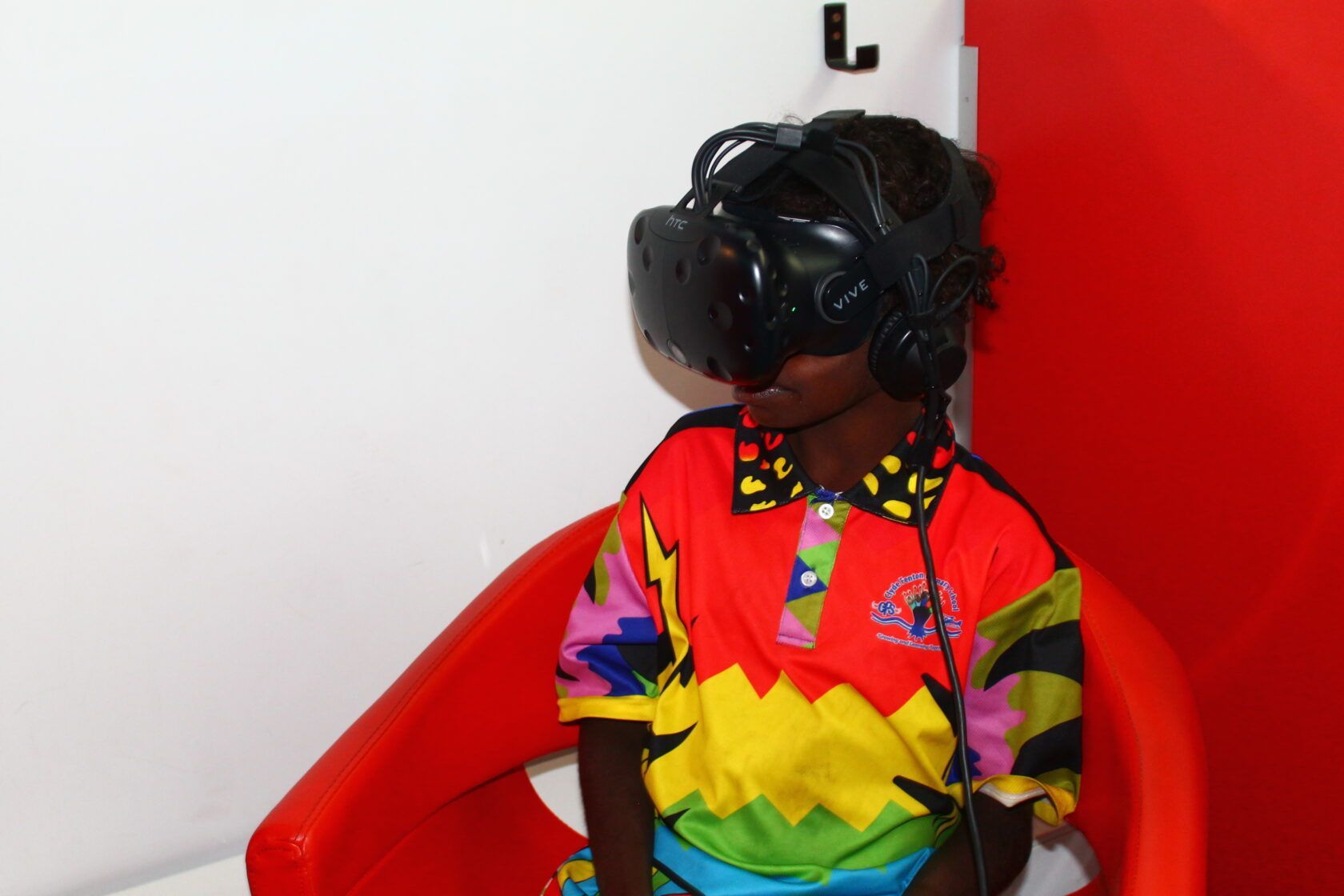A young boy wearing a virtual reality headset is sitting in a red chair