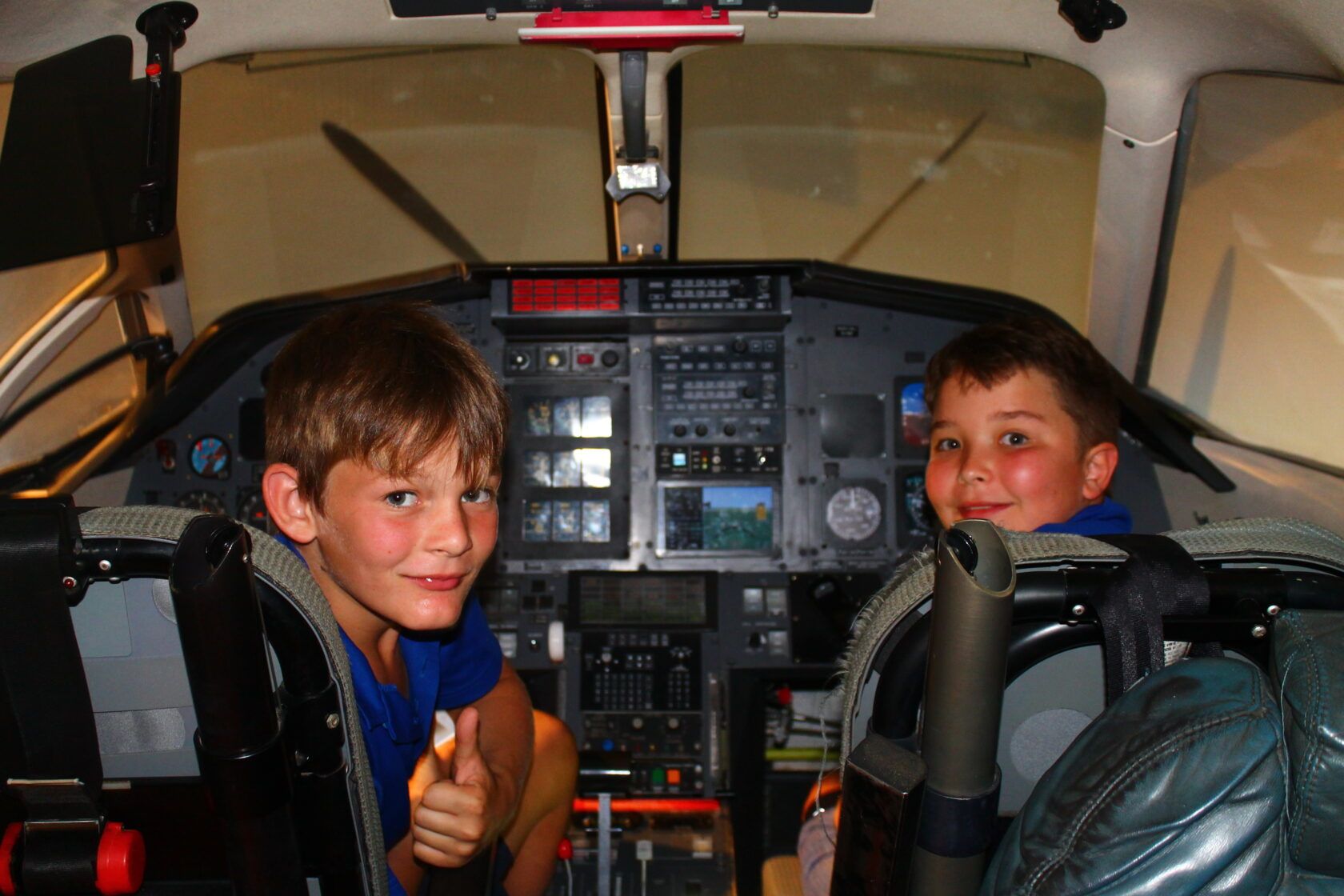Two young boys are giving a thumbs up in the cockpit of an airplane