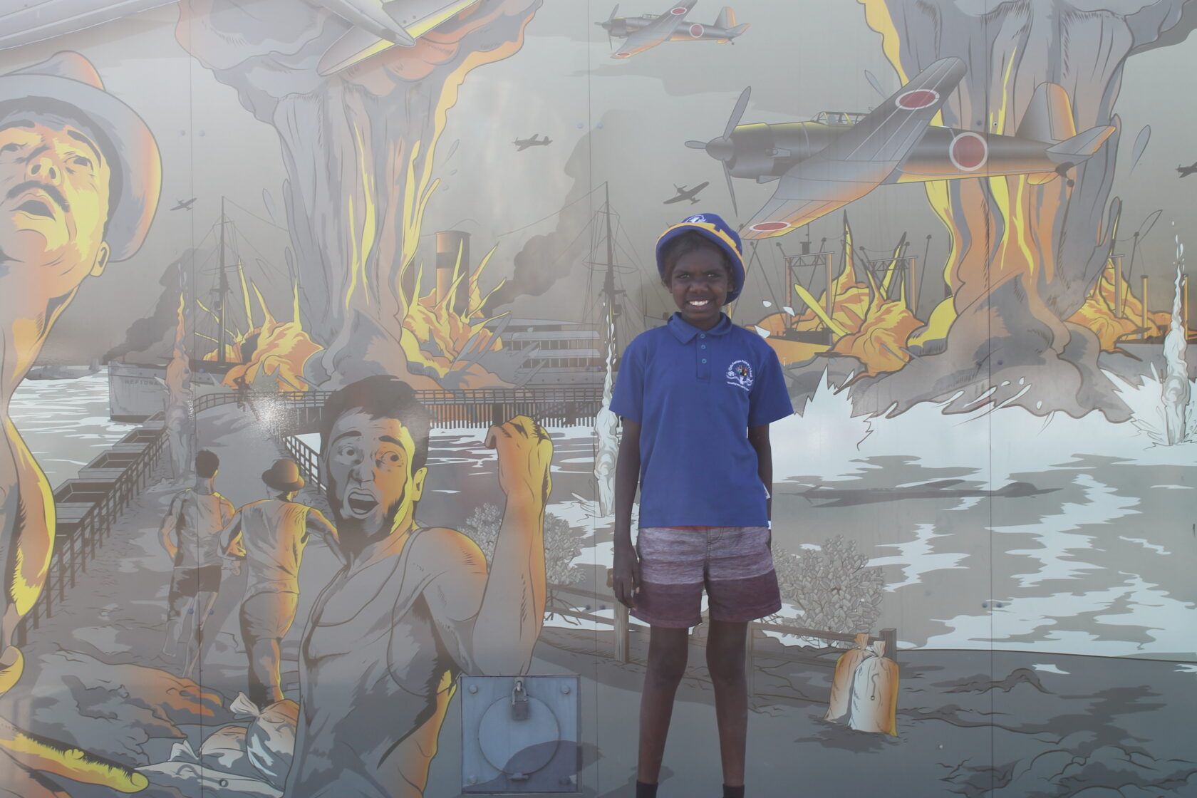 A boy in a blue shirt is standing in front of a painting.