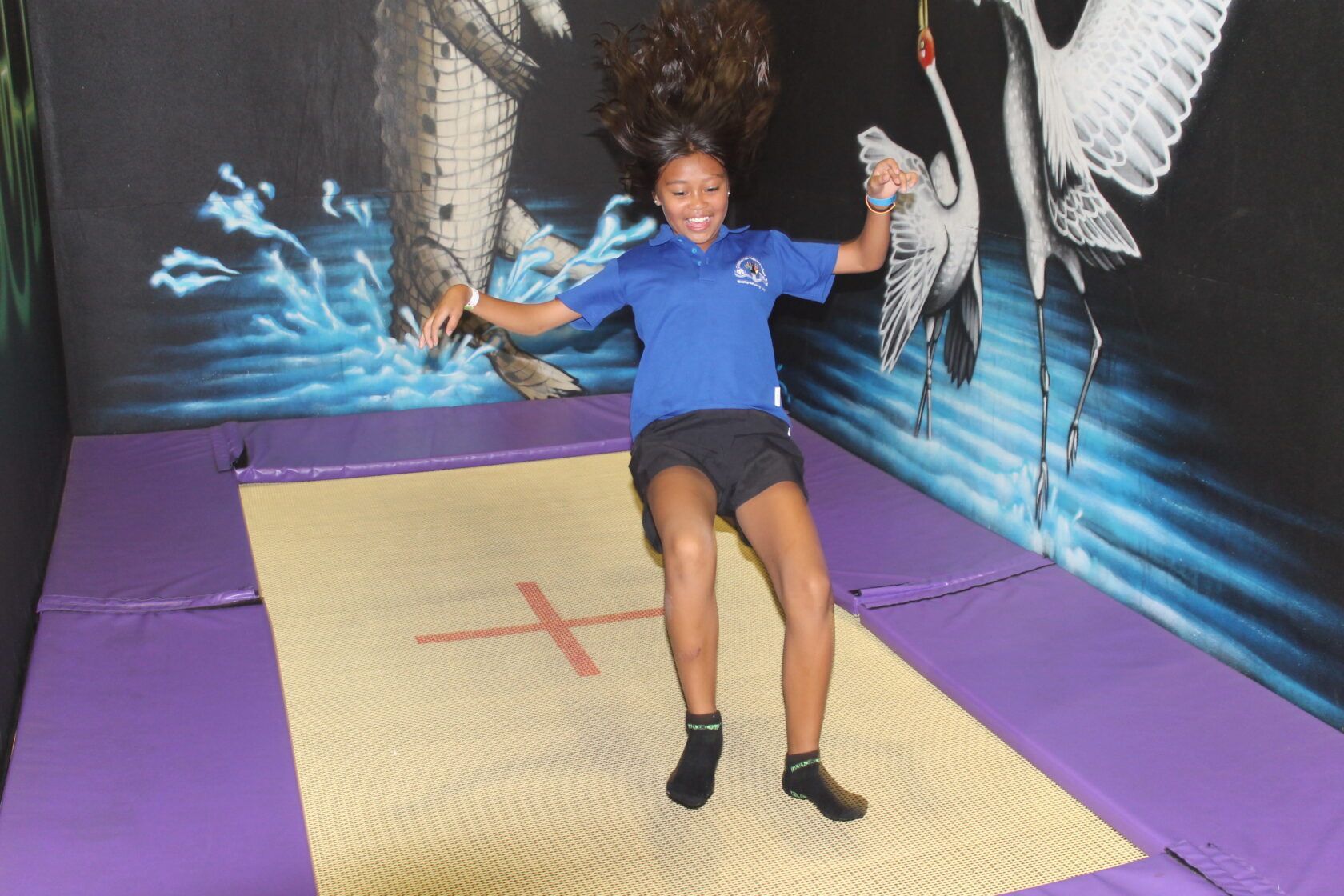 A girl in a blue shirt is sitting on a trampoline