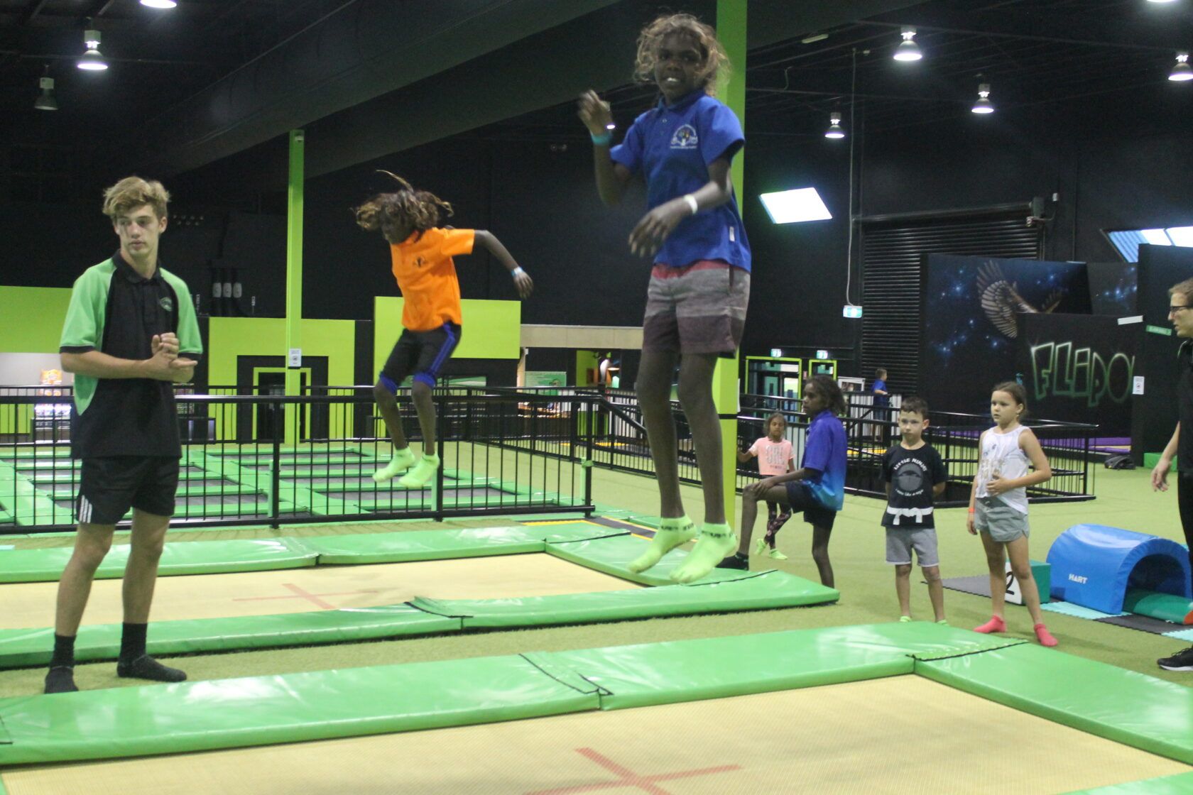 A group of people are jumping on a trampoline in a gym.