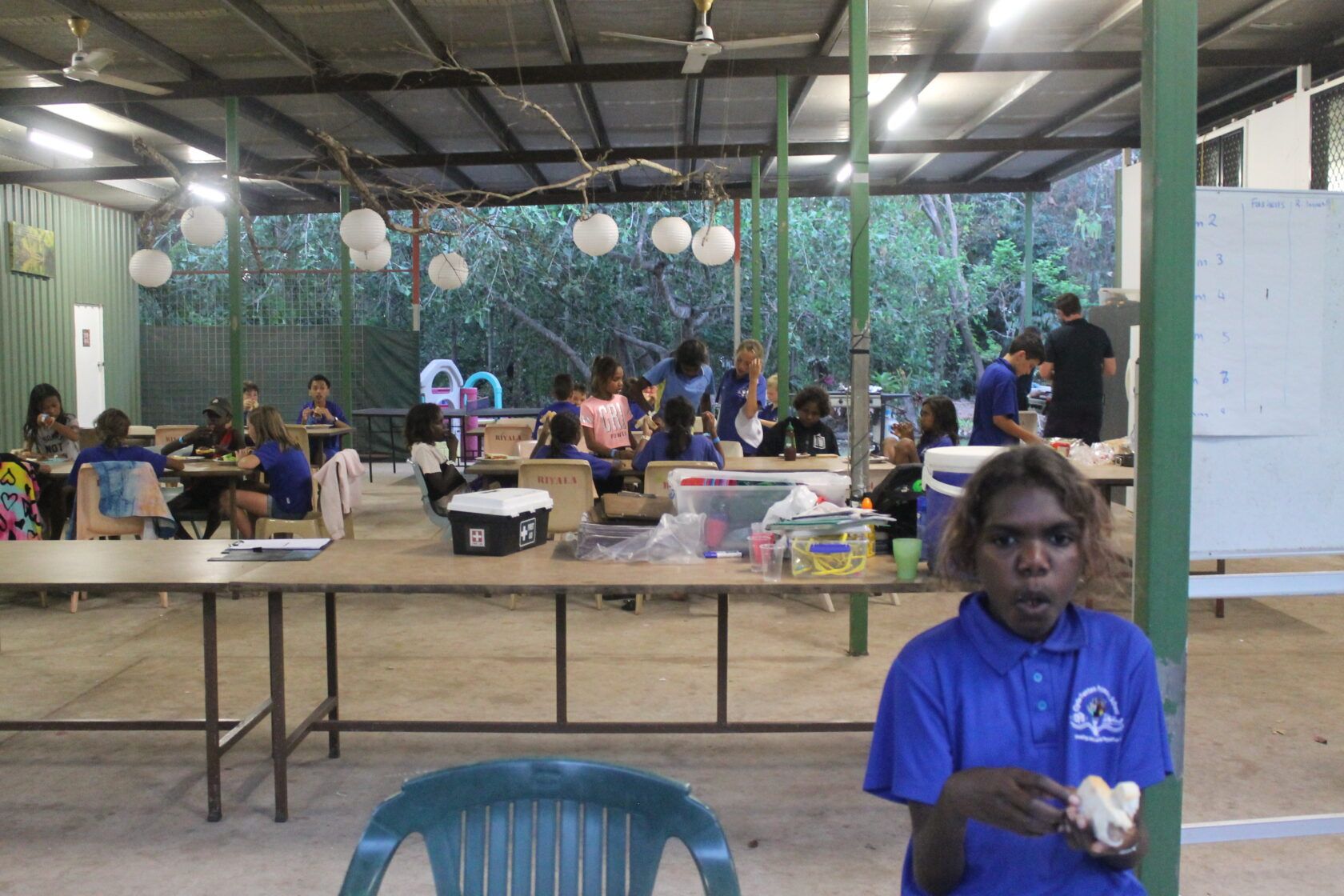 A man in a blue shirt is standing in front of a group of people sitting at tables.
