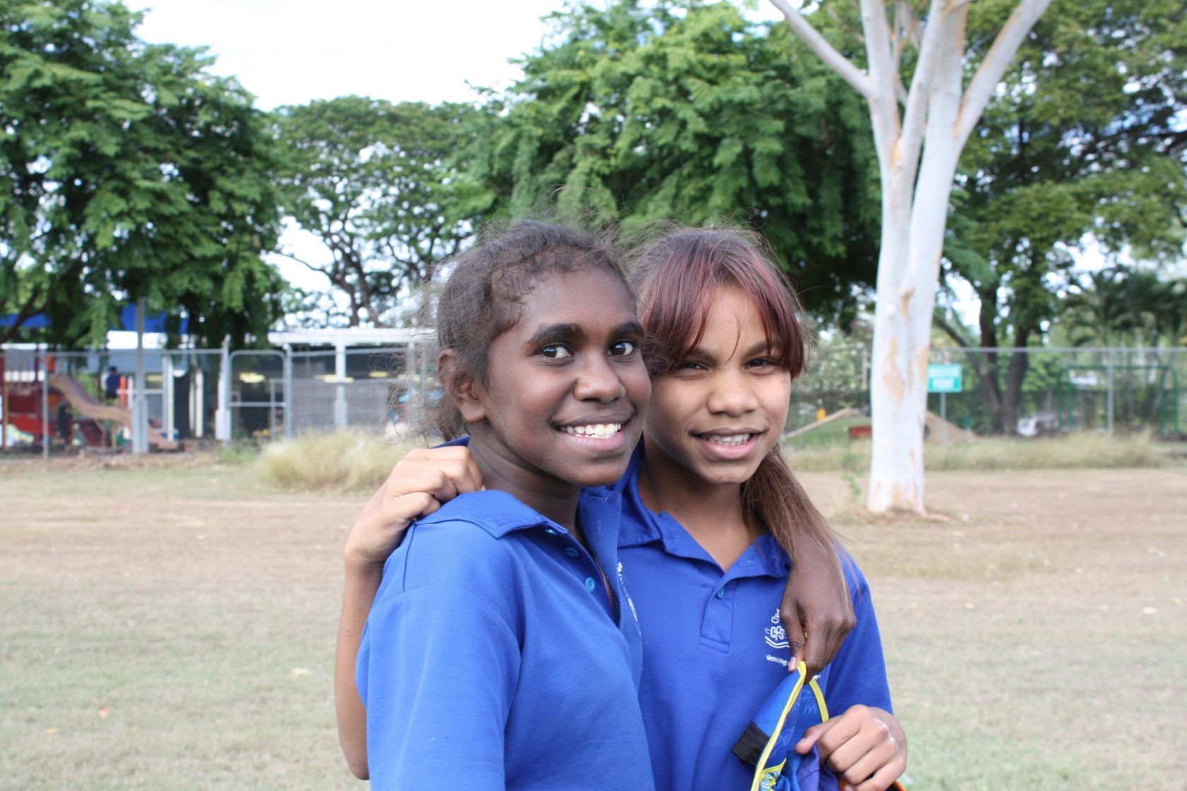 Two young girls in blue shirts are posing for a picture in a field.