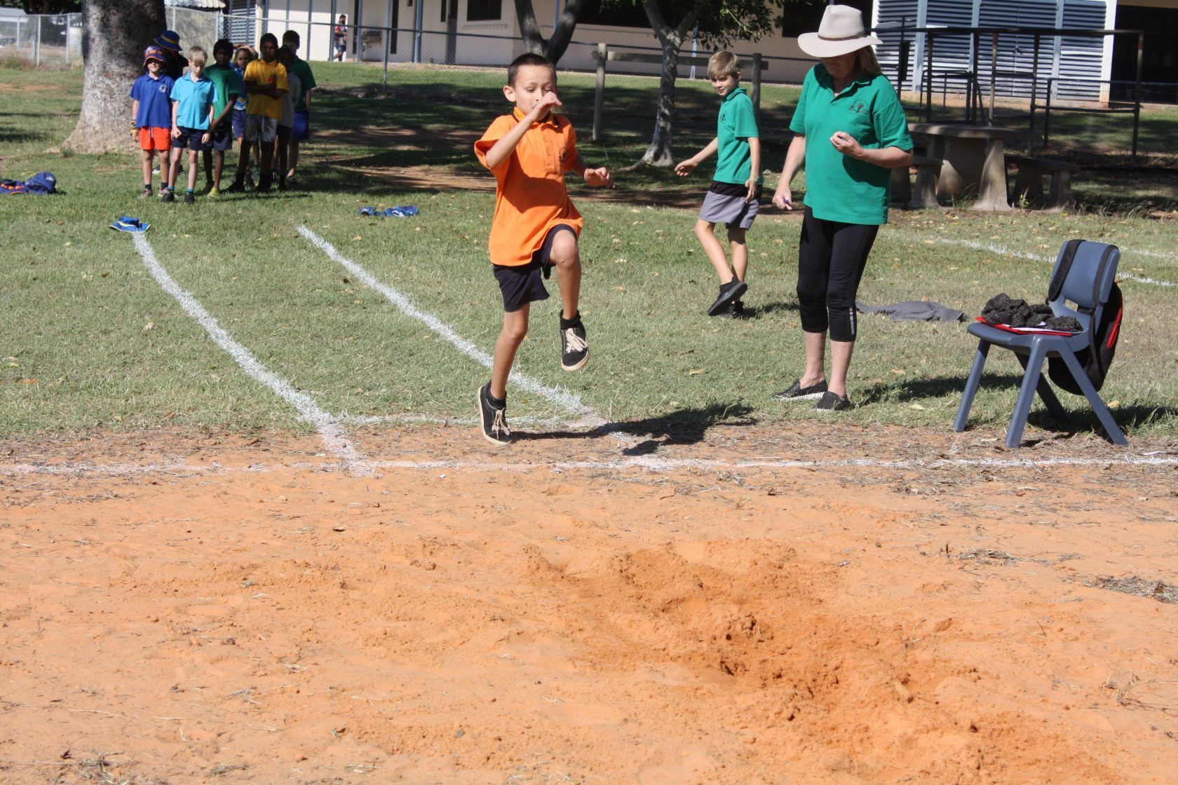 A boy in an orange shirt is jumping in the air on a dirt track.