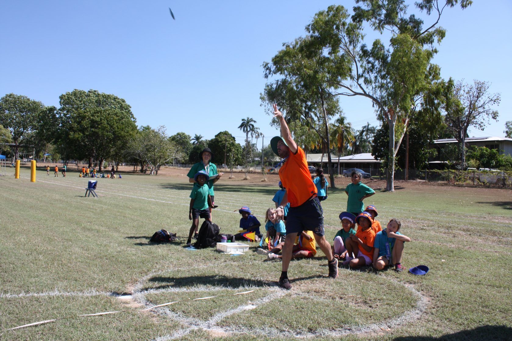 A man in an orange shirt is throwing a ball in a field