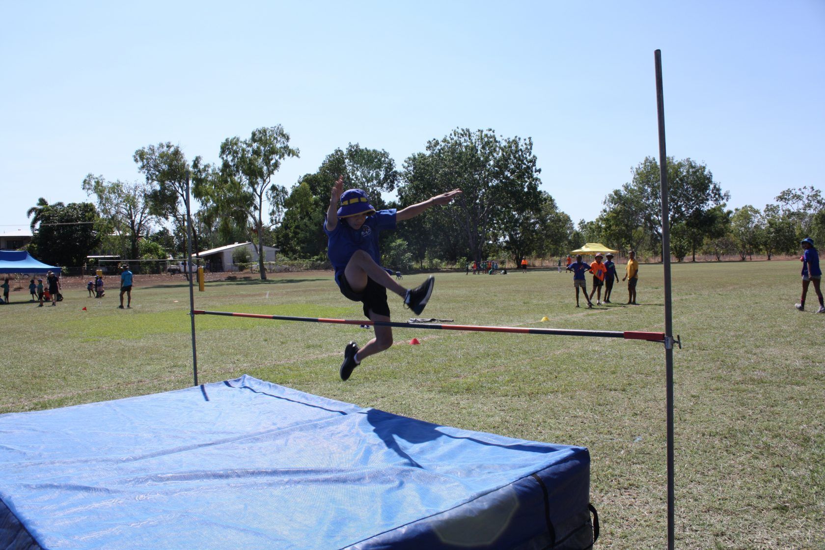A person is jumping over a blue mat in a field