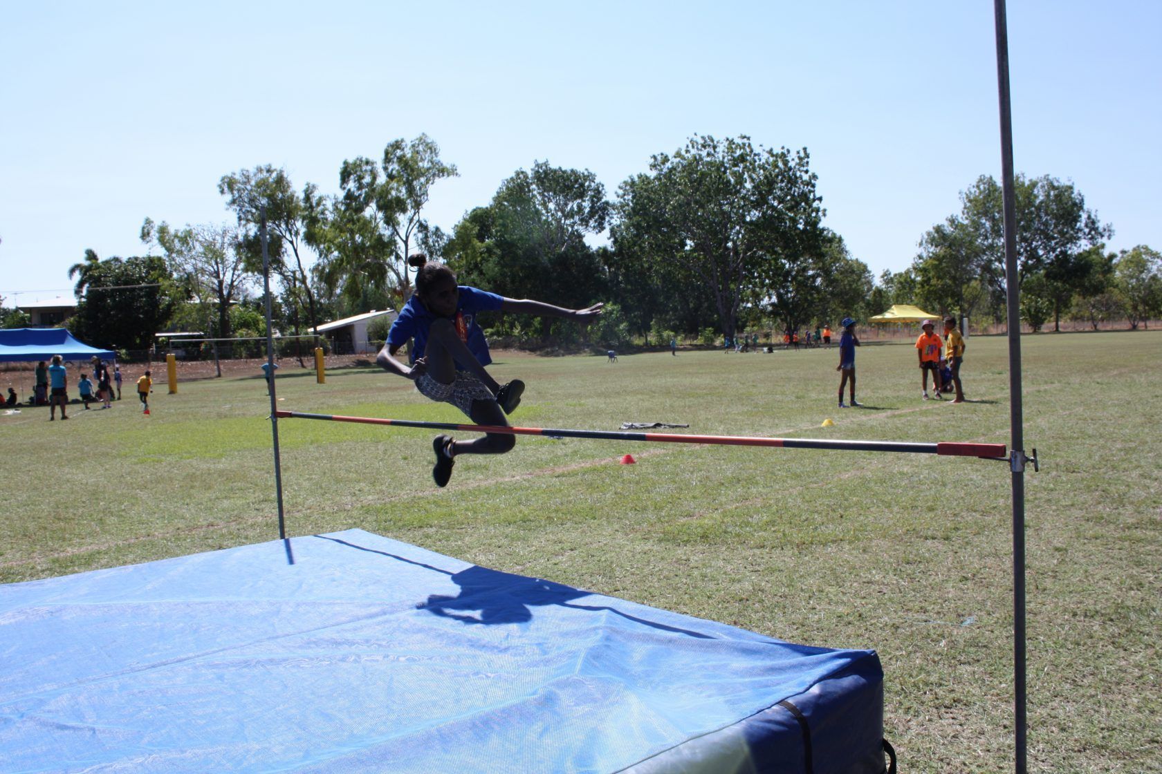 A person is jumping over a blue mat in a field