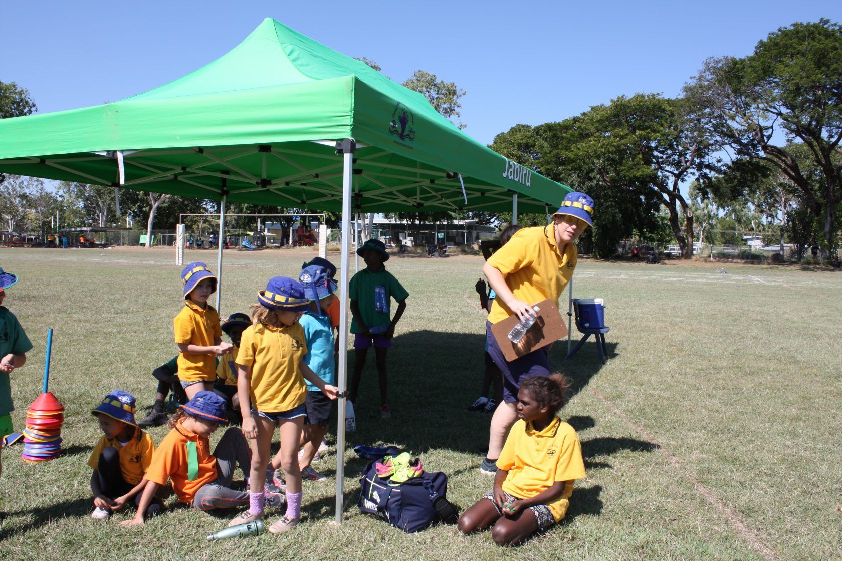 A group of children are sitting under a green tent in a field.