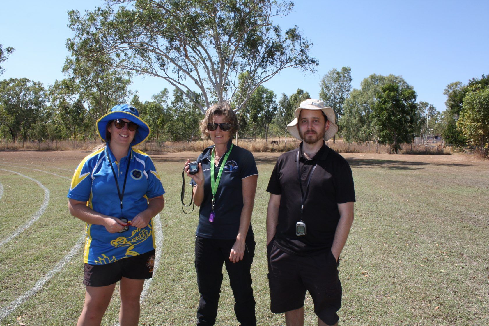 Three people standing in a field with trees in the background