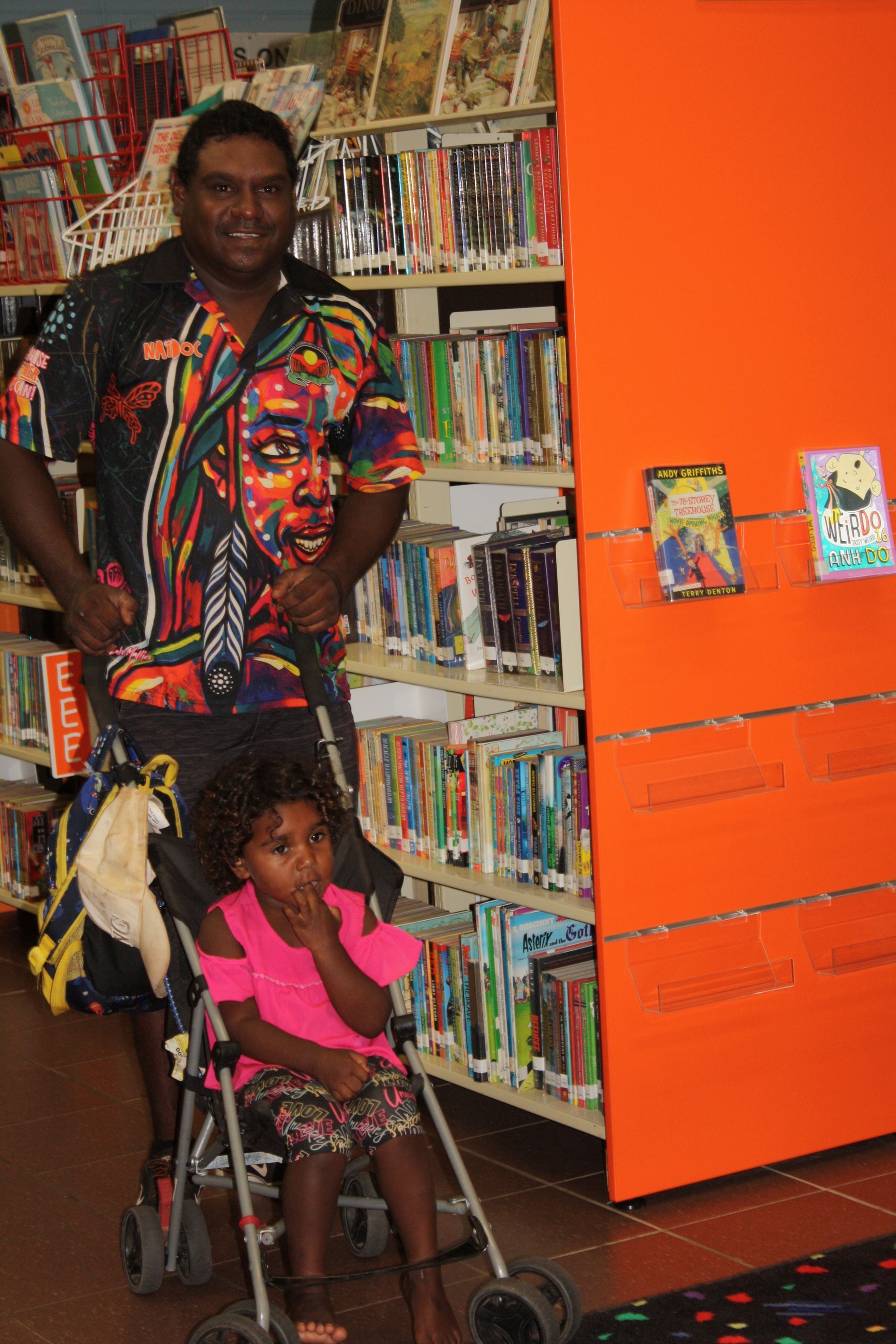 A man is pushing a stroller with a little girl in it in a library.