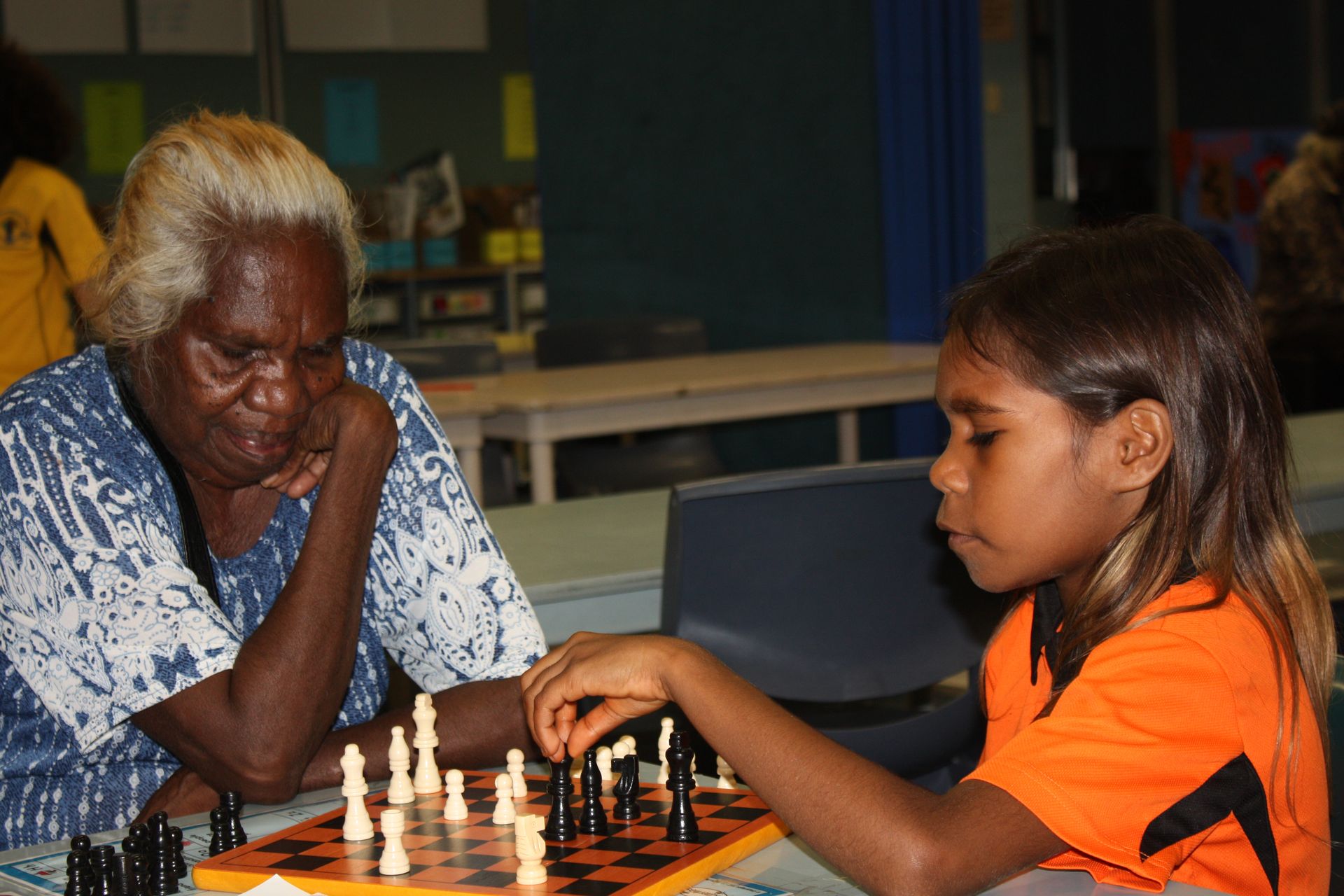 An elderly woman and a young girl are playing a game of chess.