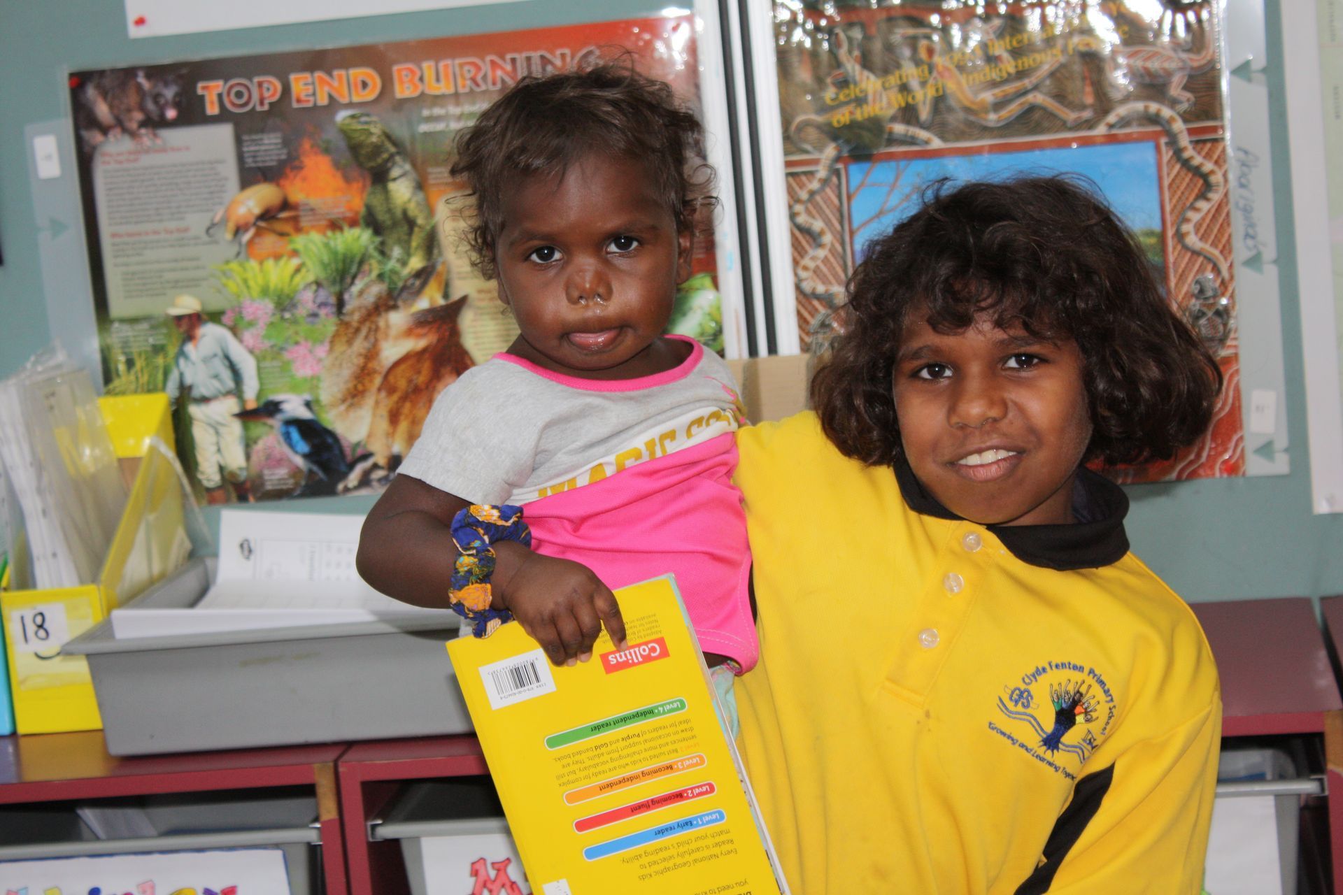 A girl in a yellow shirt is holding a little girl