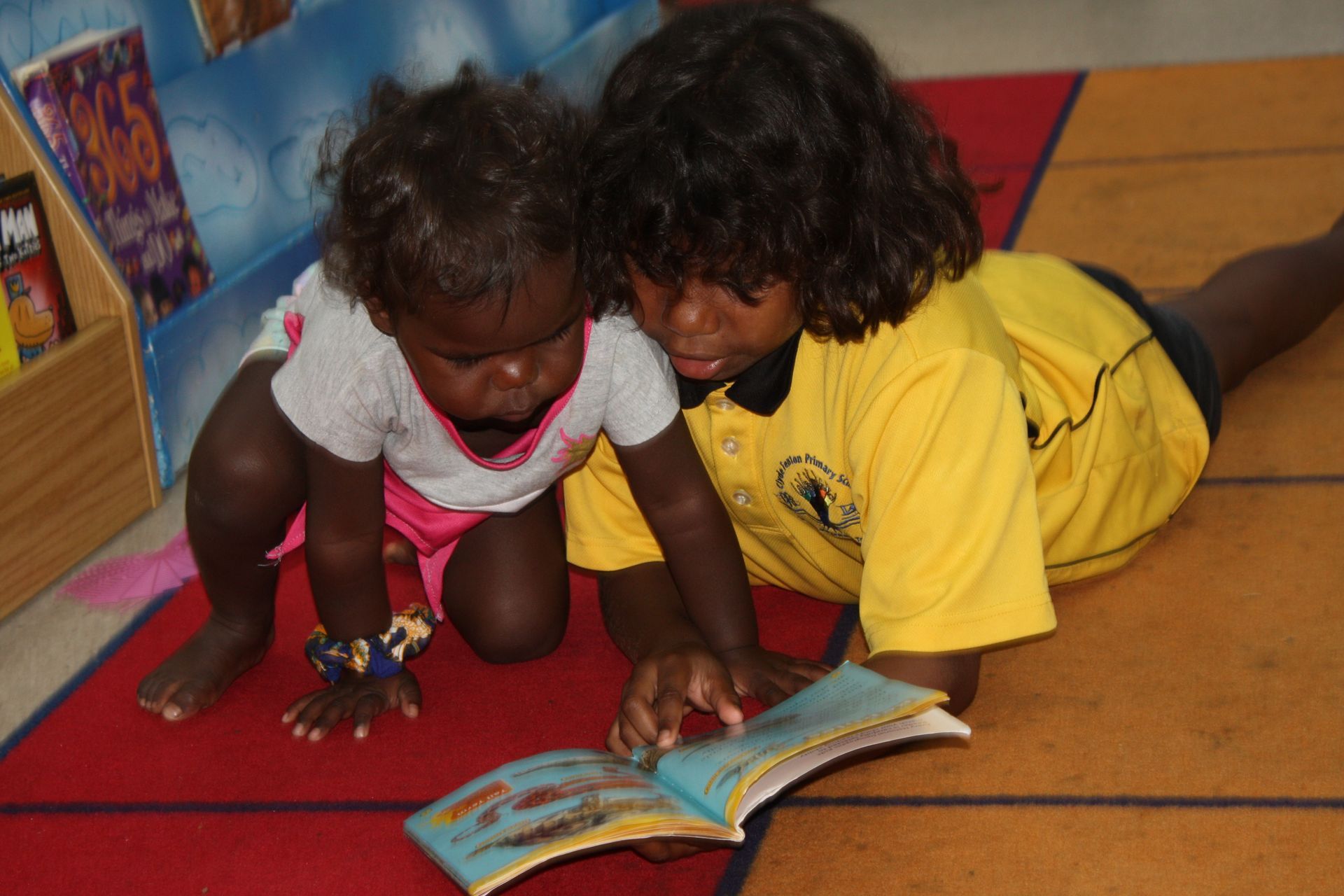 Two little girls are laying on the floor reading a book