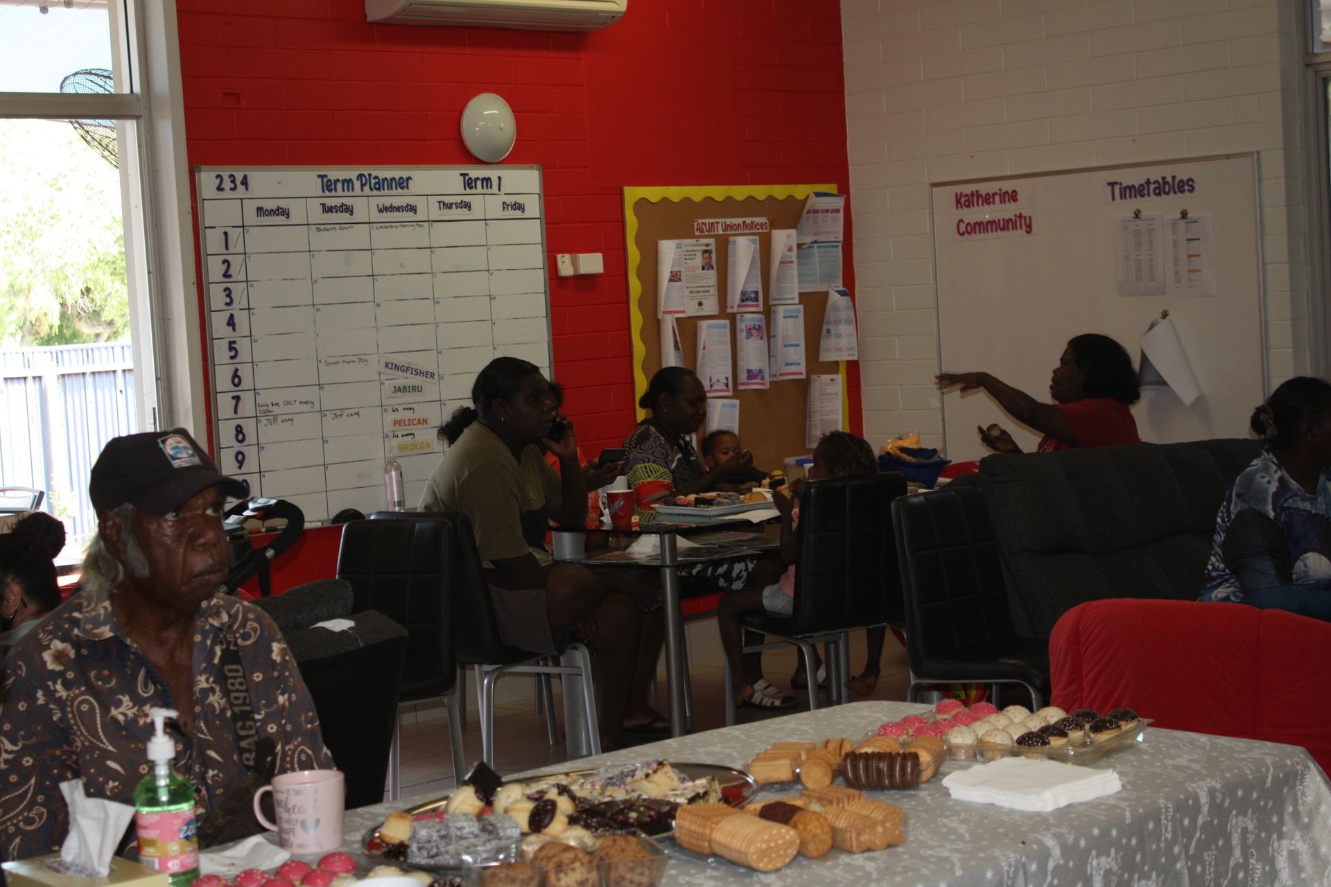 A group of people are sitting around a table with a calendar on the wall behind them