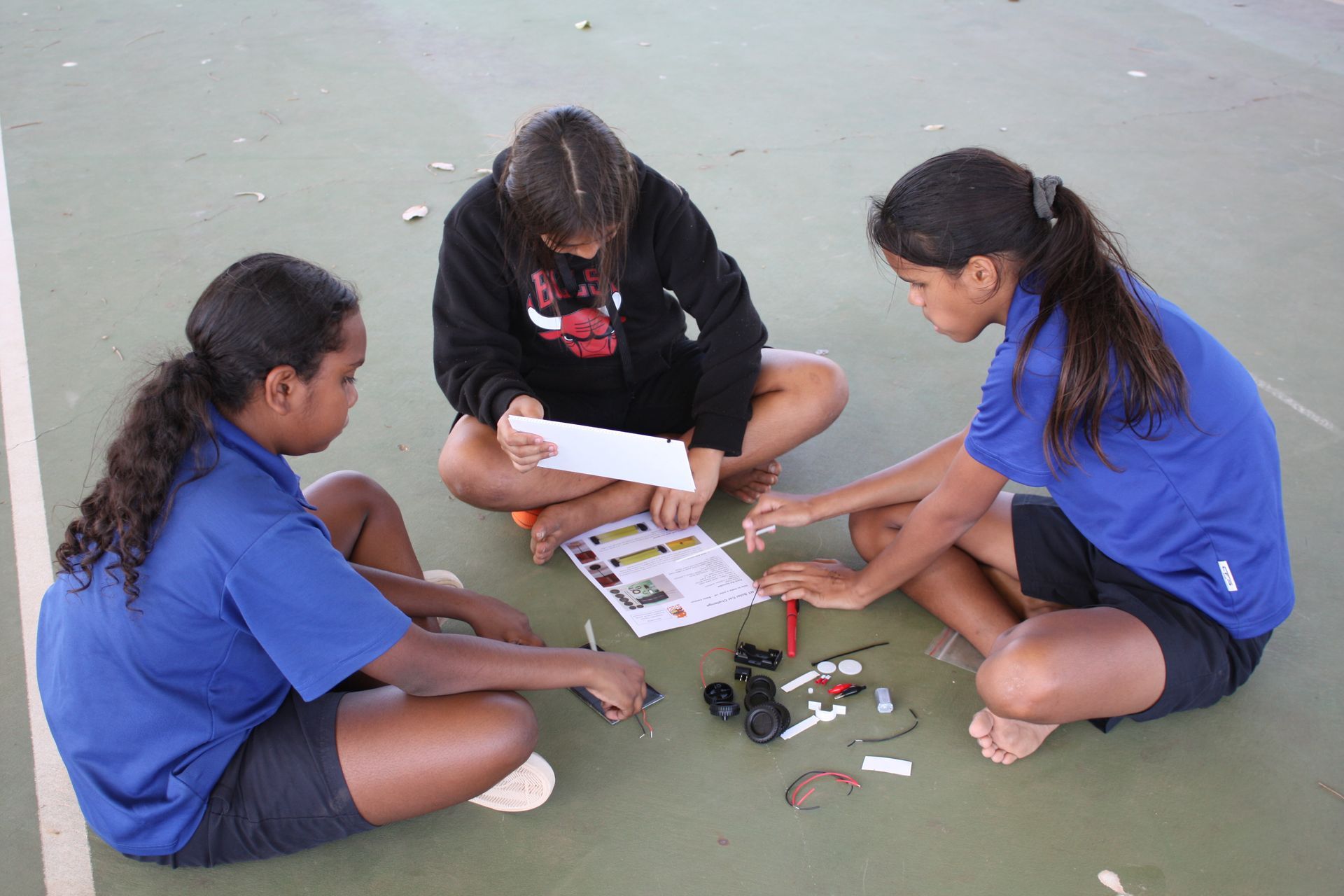 Three young girls are sitting on the ground working on a project.