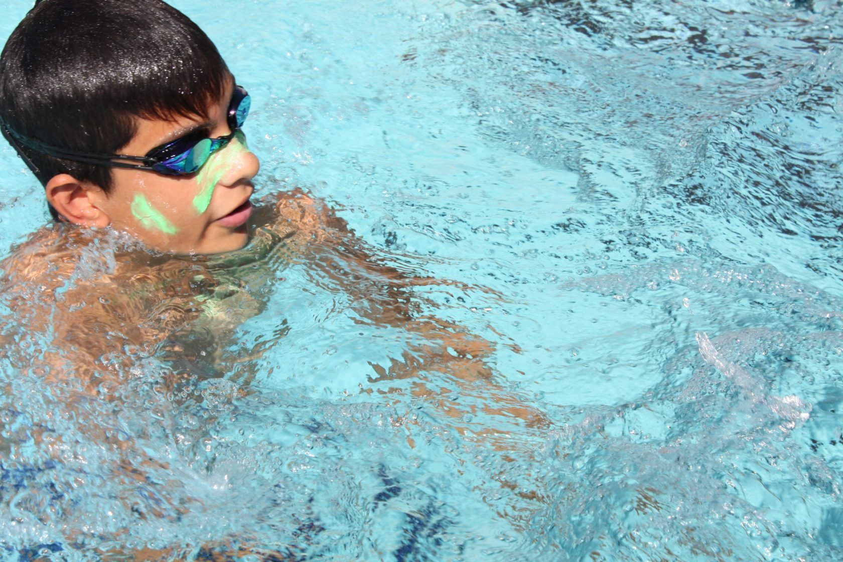 A young boy is swimming in a pool with glow in the dark paint on his face.