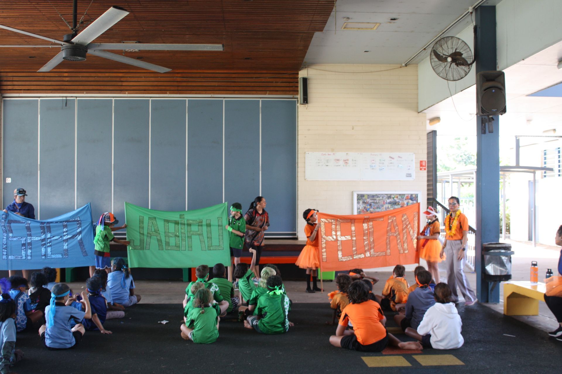A group of children are sitting on the floor in a room holding signs.