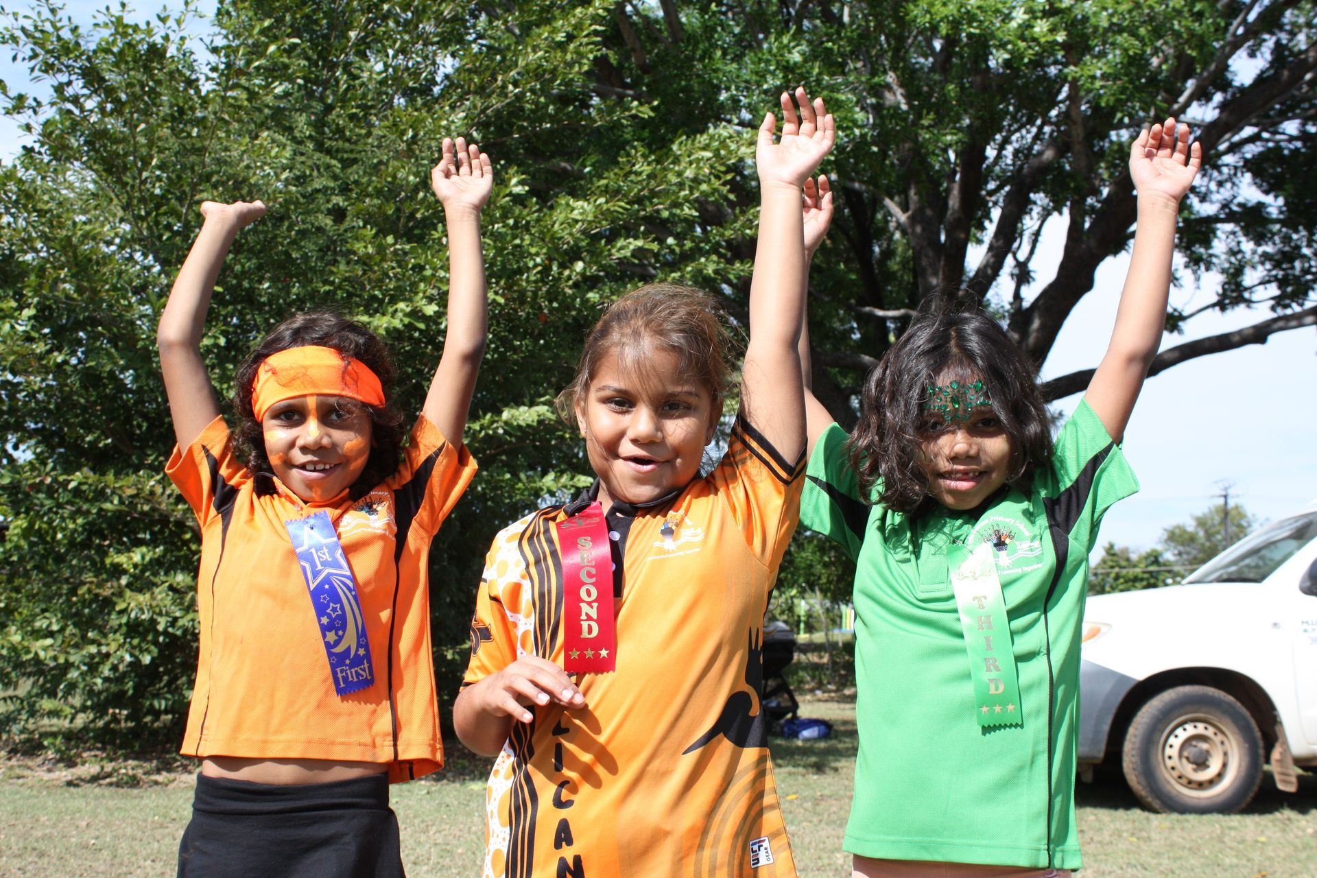 Three young girls are posing for a picture with their arms in the air