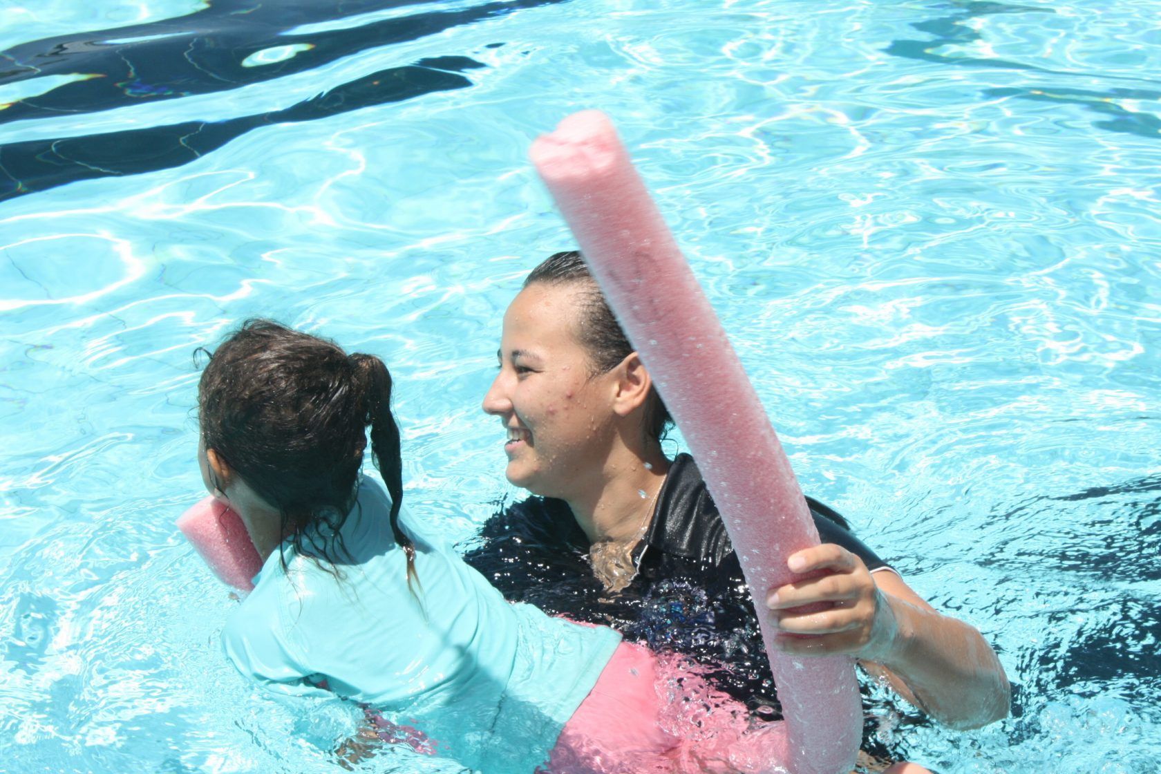 A woman is teaching a little girl how to swim in a pool.