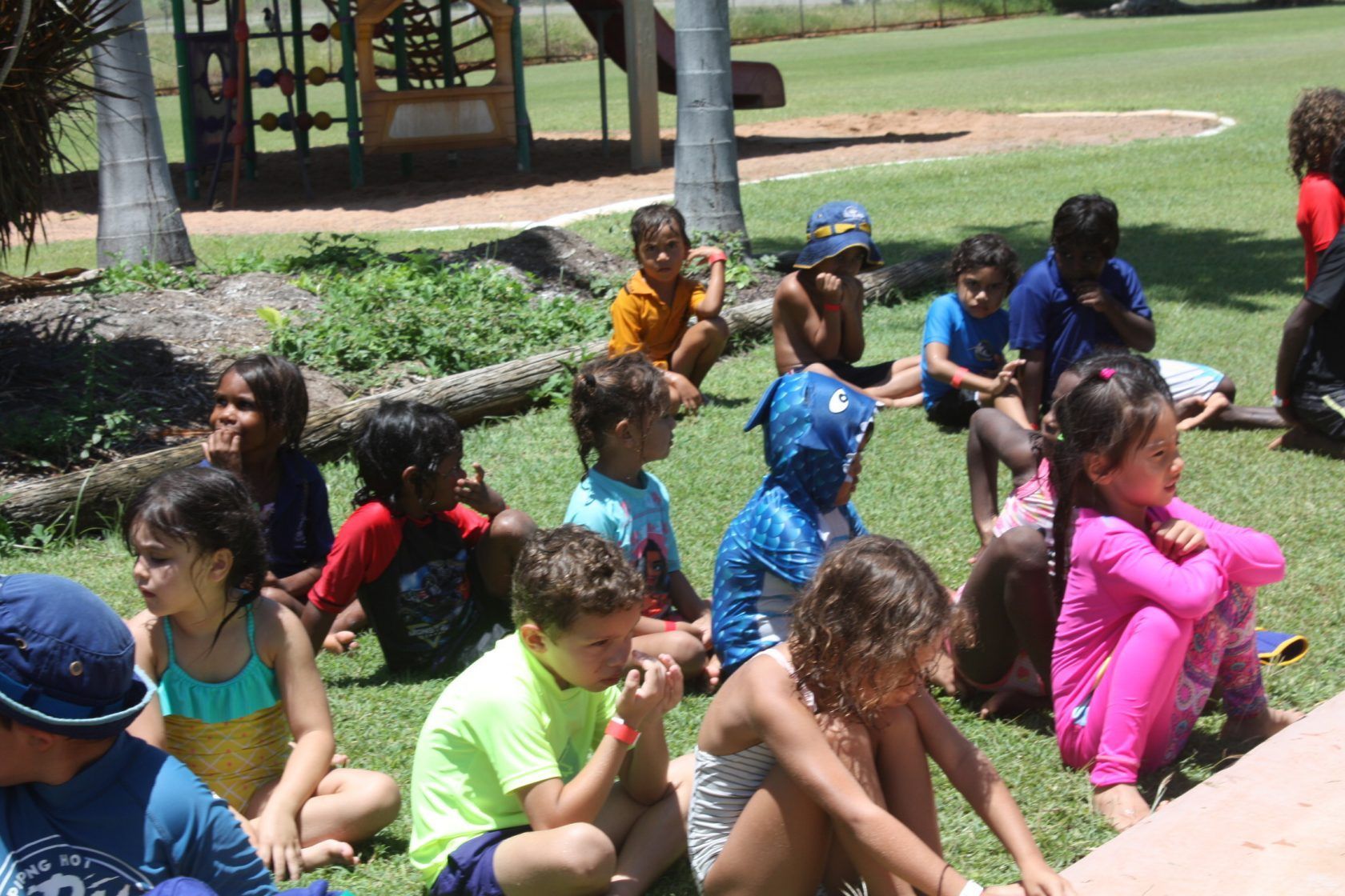 A group of children are sitting on the grass in a park