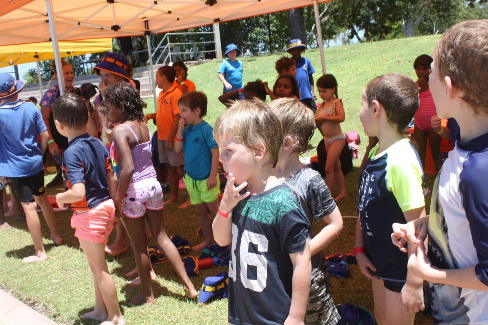 A group of children are standing under a tent and one of them has the number 16 on his shirt