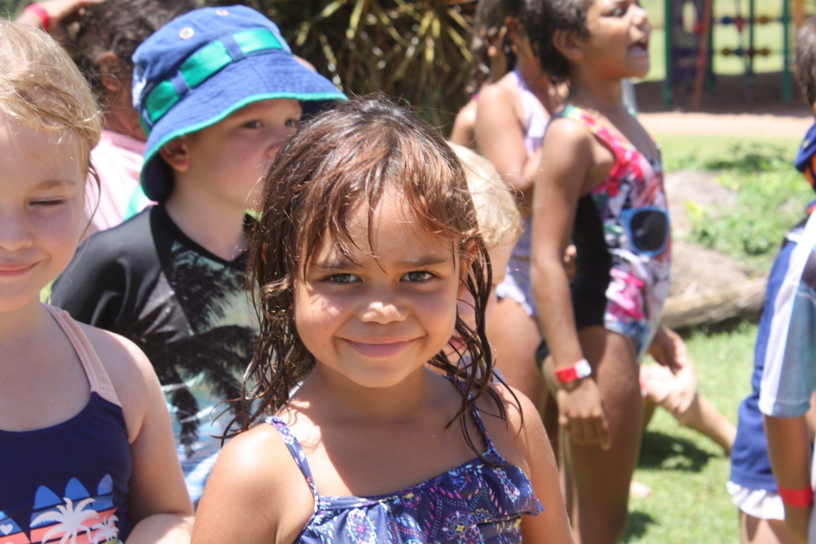 A group of children in swimsuits and hats are standing in a line.