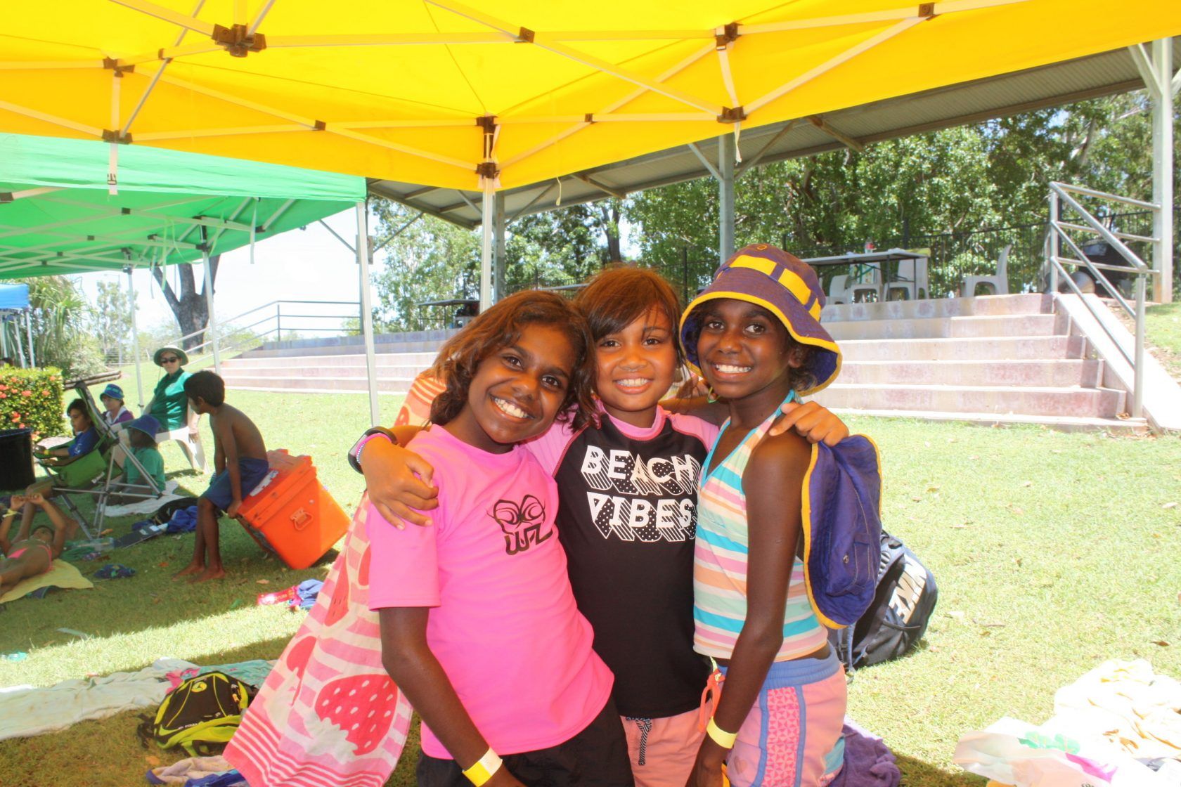 Three young girls are posing for a picture and one of them is wearing a shirt that says beach vibes