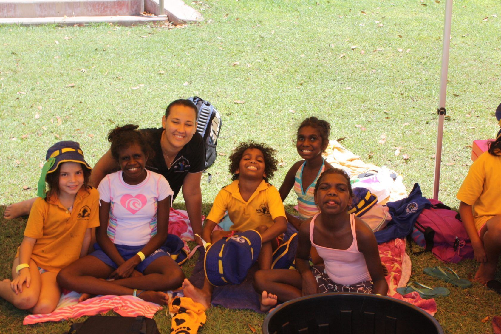 A group of children are sitting on the grass with their feet crossed