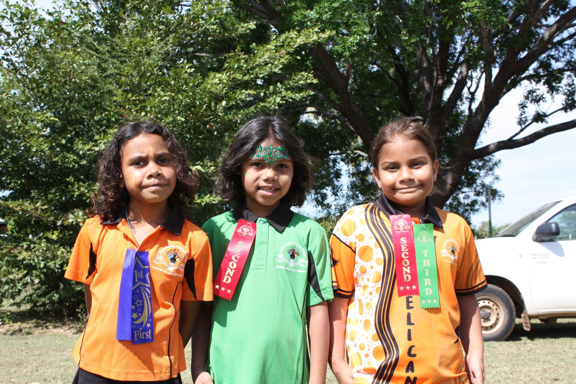 Three young girls are posing for a picture with ribbons around their necks.