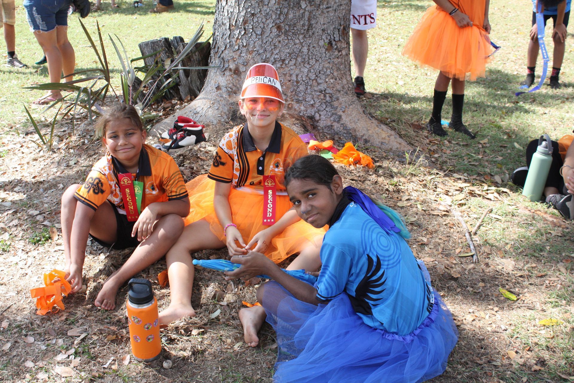 Three young girls are sitting under a tree in a park.