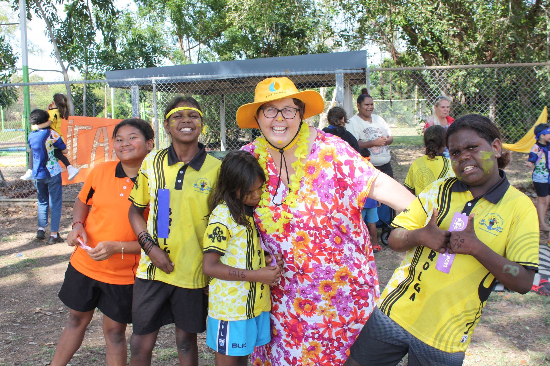 A group of children are posing for a picture with a woman in a yellow hat.