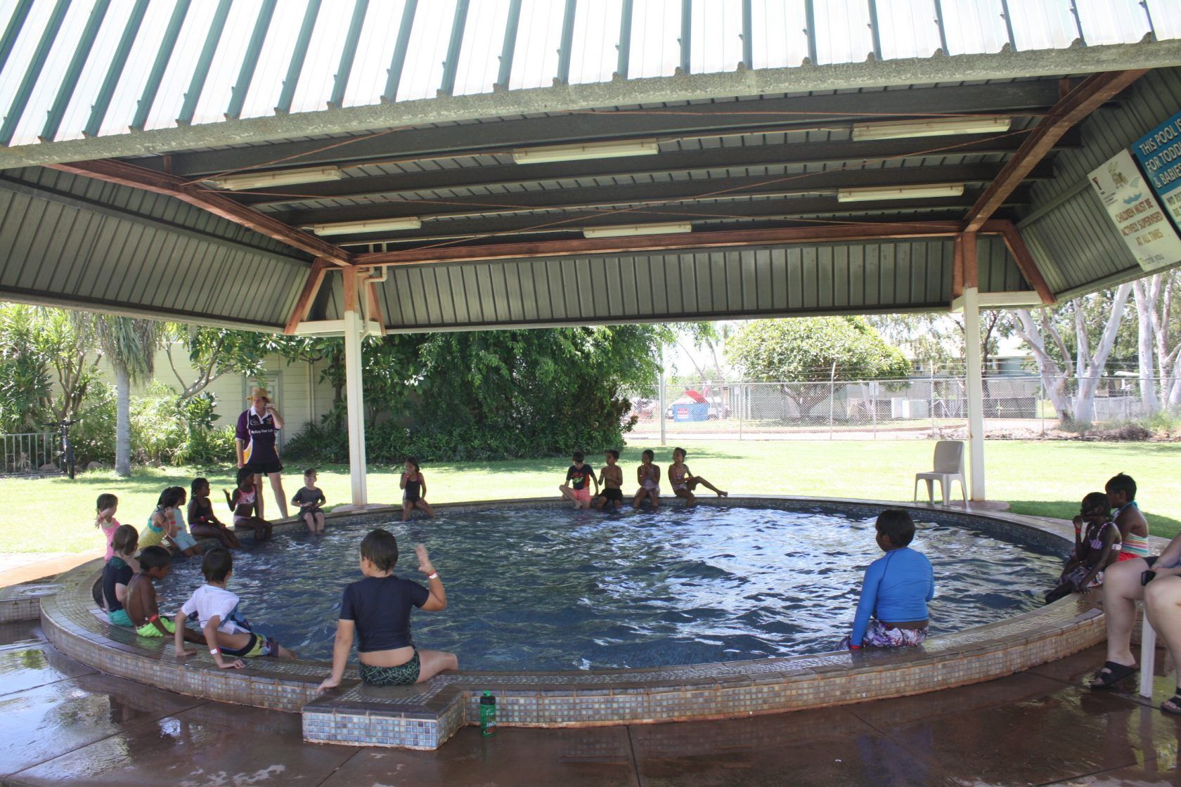 A group of children are playing in a swimming pool under a canopy.